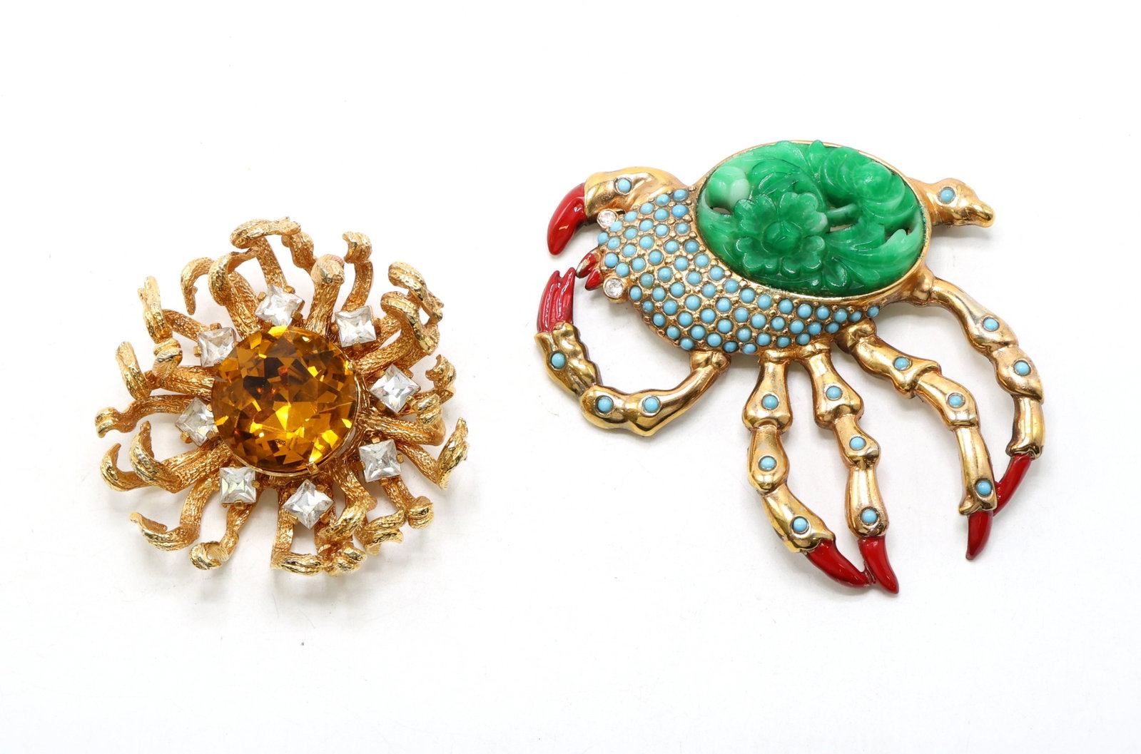Castlecliff Crab and Sunburst Brooches in Gold-Tone Setting: Castlecliff crab-shaped brooch with green carved center surrounded by enamel accents, red claw details, and gold-tone metal. Paired with a Castlecliff sunburst brooch featuring a large amber-colored c