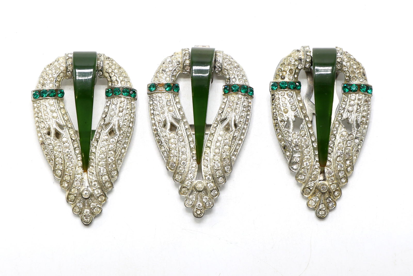 Fur Clips with Green Glass and Rhinestone Accents: Art deco fur clips featuring green glass elements set within silvertone metal frames adorned with clear rhinestones and green rhinestone accents. Includes loose rhinestones. Measures 2.5”h