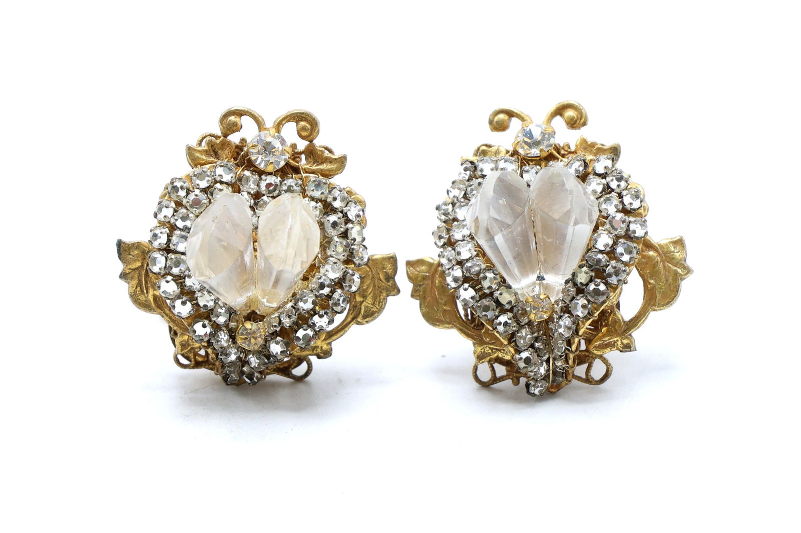 Miriam Haskell Clip-On Earrings with Rhinestone Accents: Miriam Haskell clip-on earrings in gold-tone metal featuring ornate scrollwork and floral motifs. Heart-shaped clear rhinestones are encircled by a row of smaller round rhinestones. Earrings measure 1