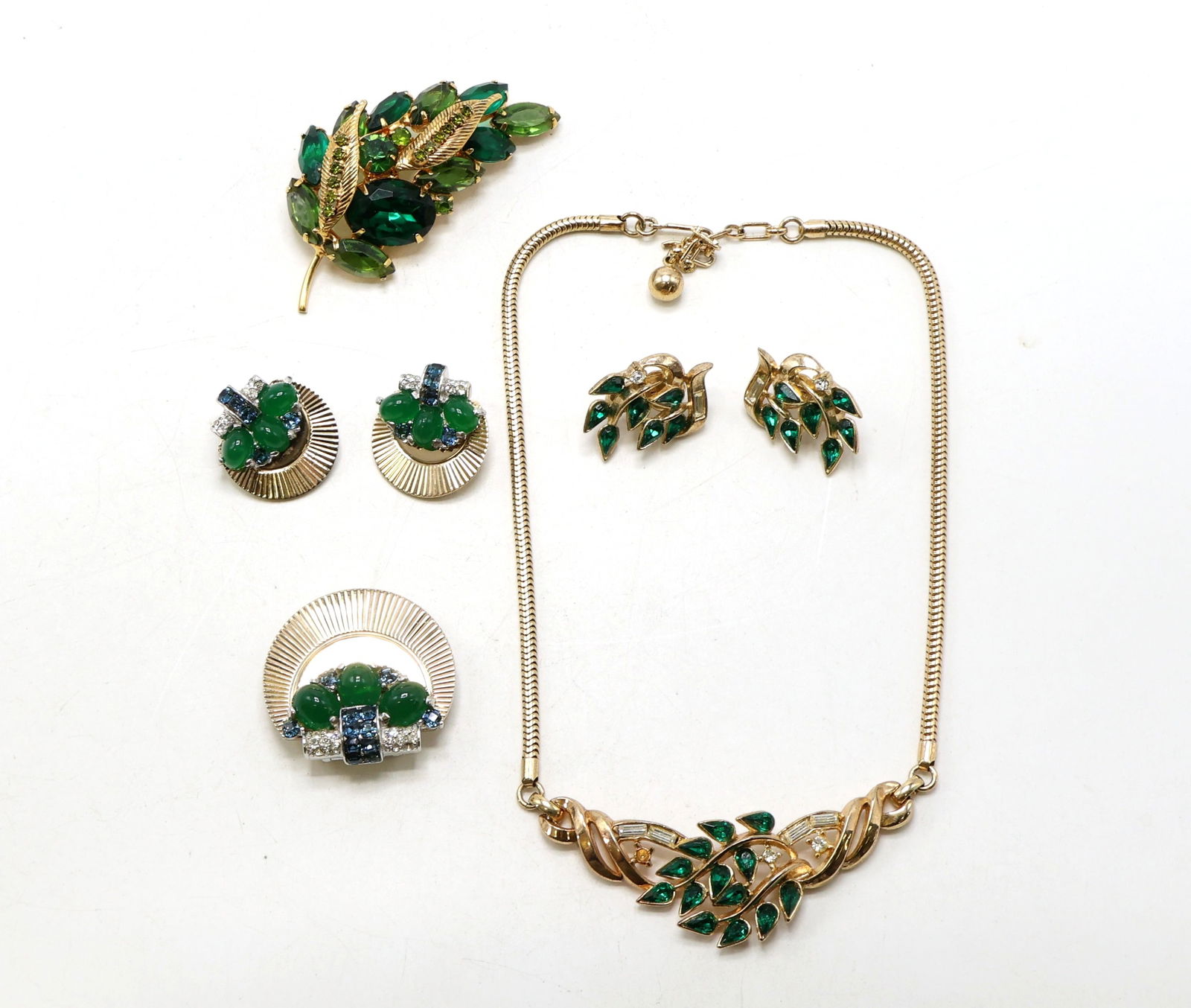 Trifari and Boucher Jewelry Collection: Trifari gold-tone necklace and matching clip-on earrings with green navette rhinestones, Trifari leaf brooch with green rhinestones, and Boucher circular brooch with matching clip-on earrings showcasi