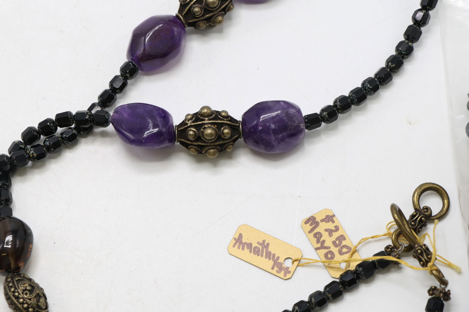 Beaded Necklaces: Necklaces including a strand with green, brown, and blue glass beads, a second with black faceted beads, amethyst and bronze-tone details, and a third featuring a metal chain with amber-tone bead acce