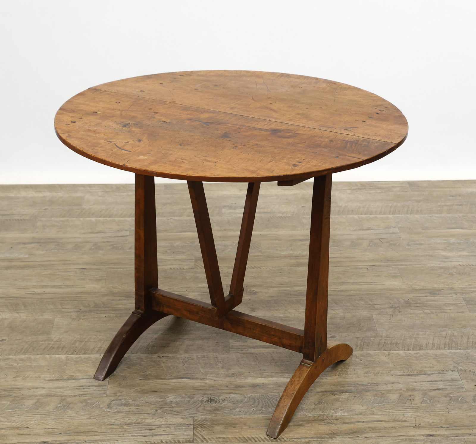 French Tilt-Top Wine Tasting Table: Walnut with an oval top, peg construction, swing pedestal supports, tapered legs, arched trestle feet. 27.5"h (43"h tilt) x 34"w