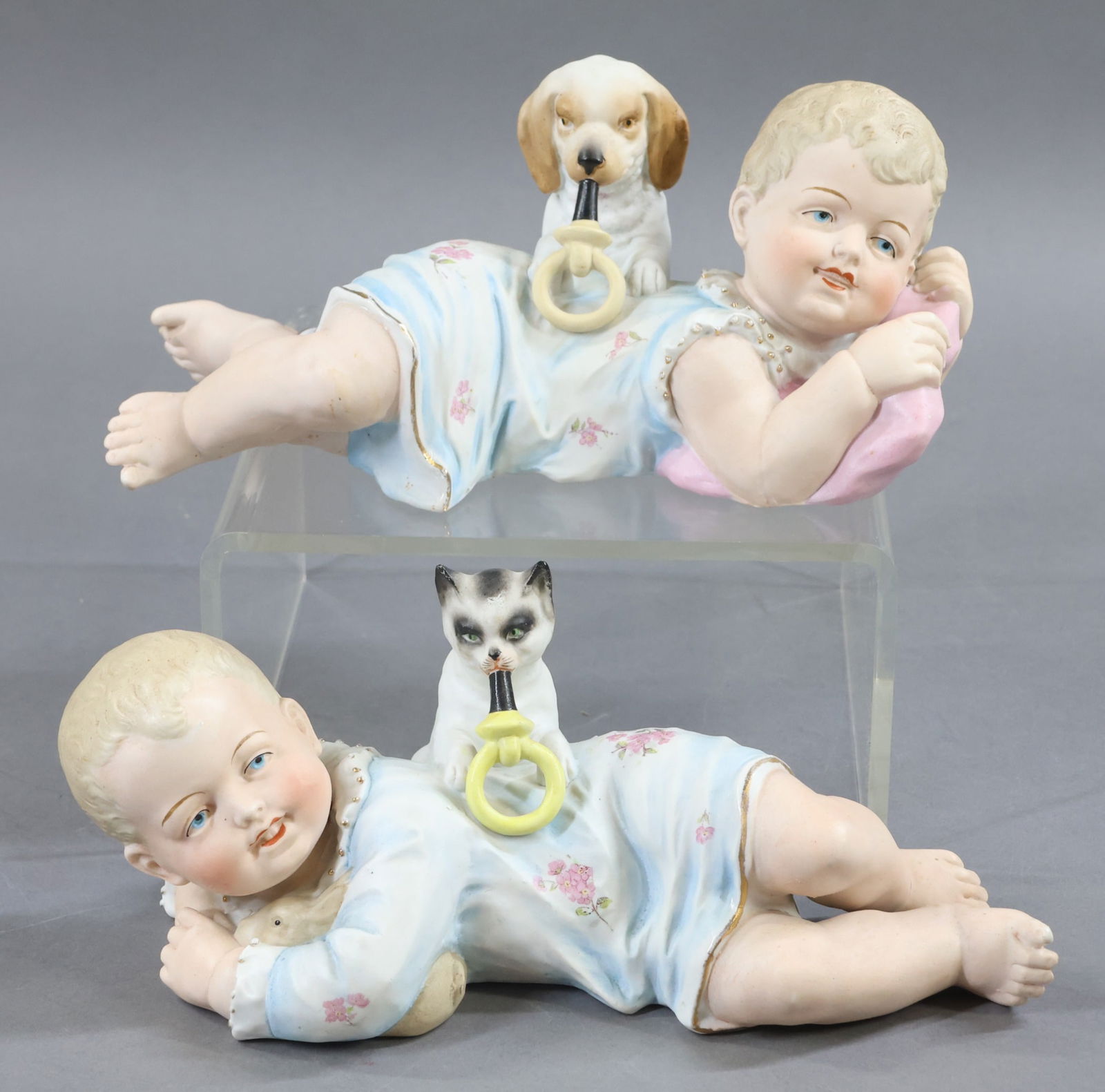 FIGURINES.: Pair of porcelain baby figurines marked 2149. Each one is 5" T x 10" L. Little girl with puppy, is holding a pink pillow. Little boy is cuddling a rabbit and has a cat. Each animal is leaning with the