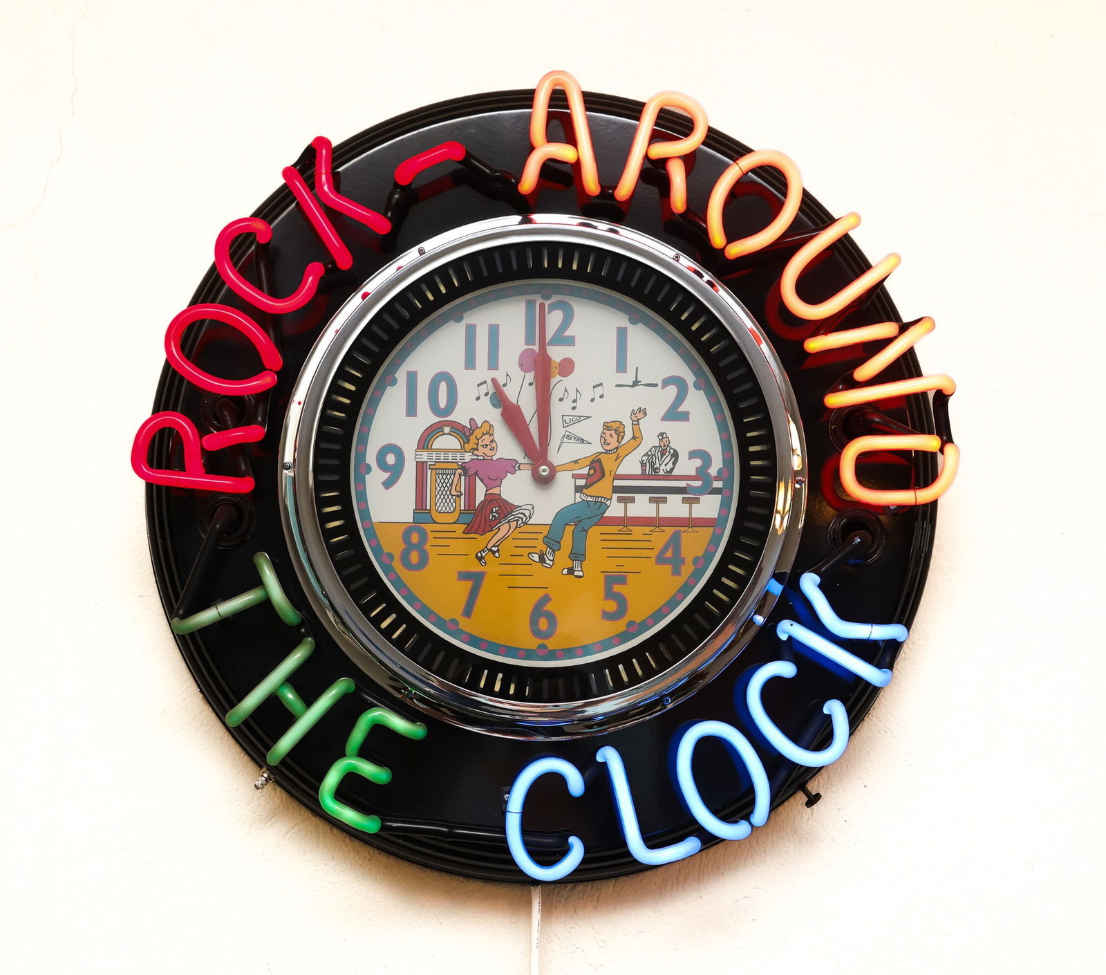 “Rock Around the Clock" Neon Wall Clock: Retro style neon wall clock with colorful tubing in red, orange, green, and blue spelling out “Rock Around the Clock.” The dial is a jukebox scene with a couple dancing to 1950s rock and roll.