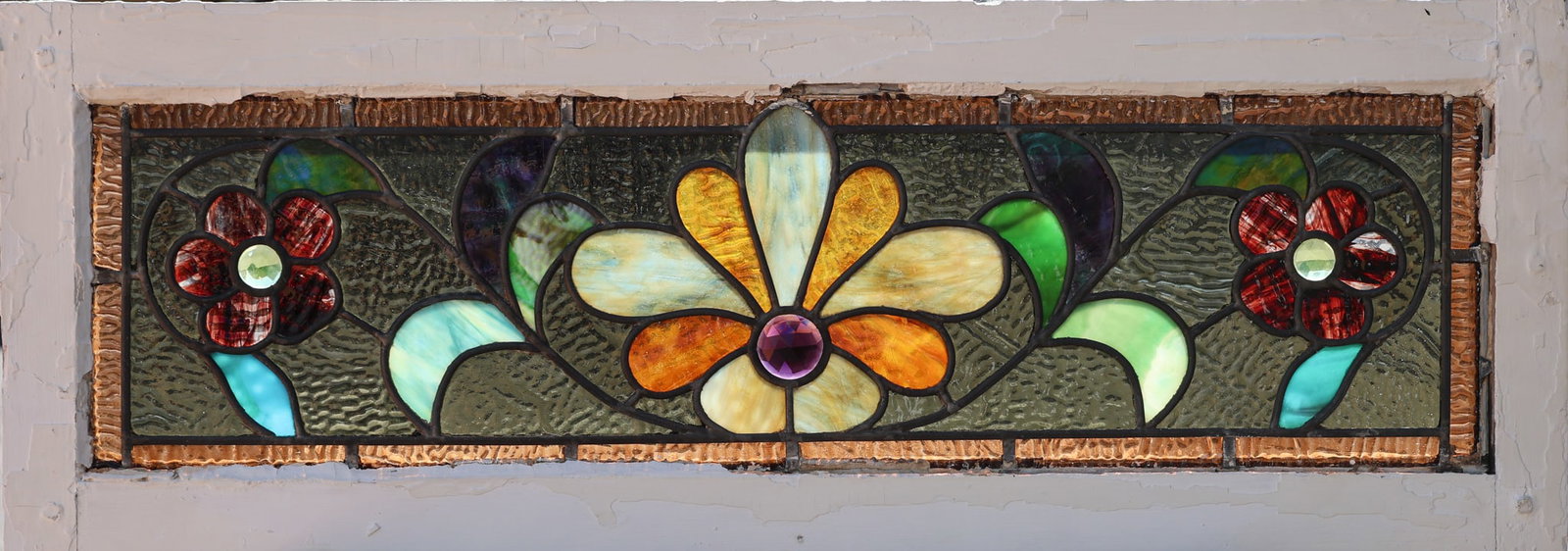 Stained & Leaded Glass Transom Panel: Framed slag and textured glass with jeweled glass accents. Stylized fan motif in center, flowers and vines complete the composition, orange/brown border on all sides. 11.25"h x 32.25"w x 1.5"d