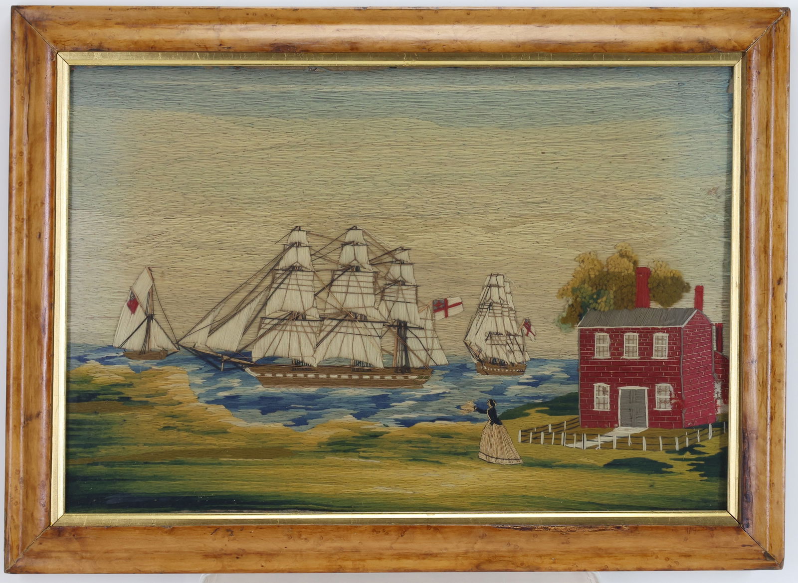British Sailor's Woolie Embroidery: British sailor’s woolwork embroidery depicting a Royal Man-o-War ship in full sails, smaller vessels at the bow and stern. A woman is standing on the grassy shoreline looking out into the water, sig