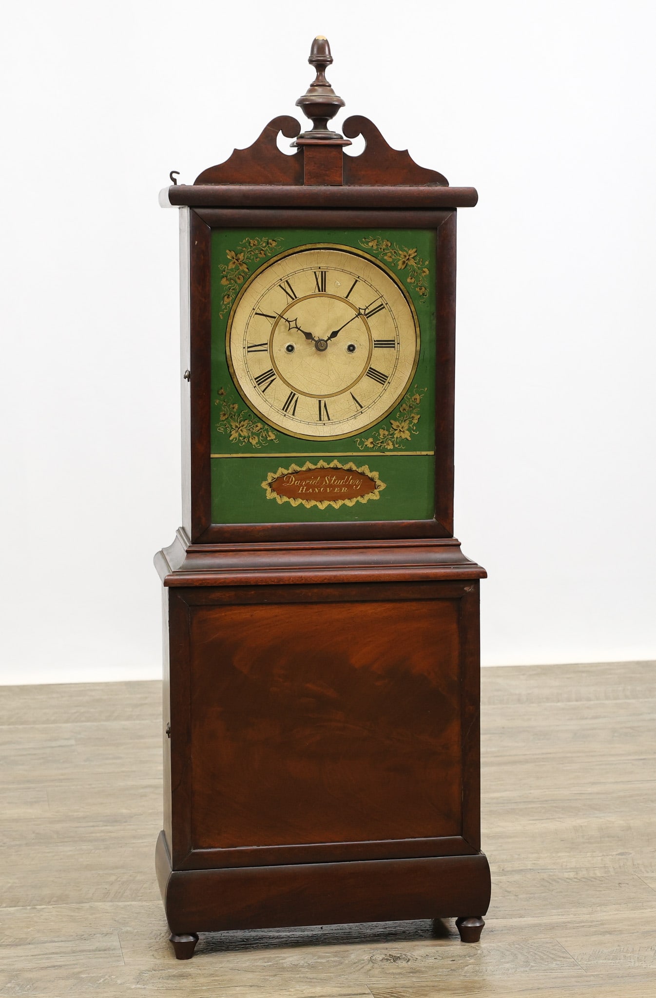 David Studley Hanover, Massachusetts Shelf Clock: Mahogany case having a broken arch pediment, eglomise hood tablet signed "David Studley Hanover", molded and paneled waist door, plinth base on turned tapered feet. Eight-day brass movement. Early 19t