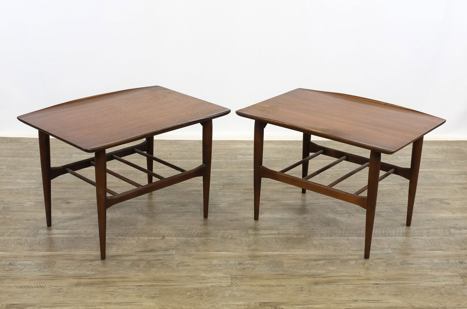 Bassett Side Tables: Danish Modern style pair of walnut side tables with rectangular tops featuring slightly rounded and upturned edges to two sides, lower tiers with round slats and shaped stretchers, raised on cigar leg