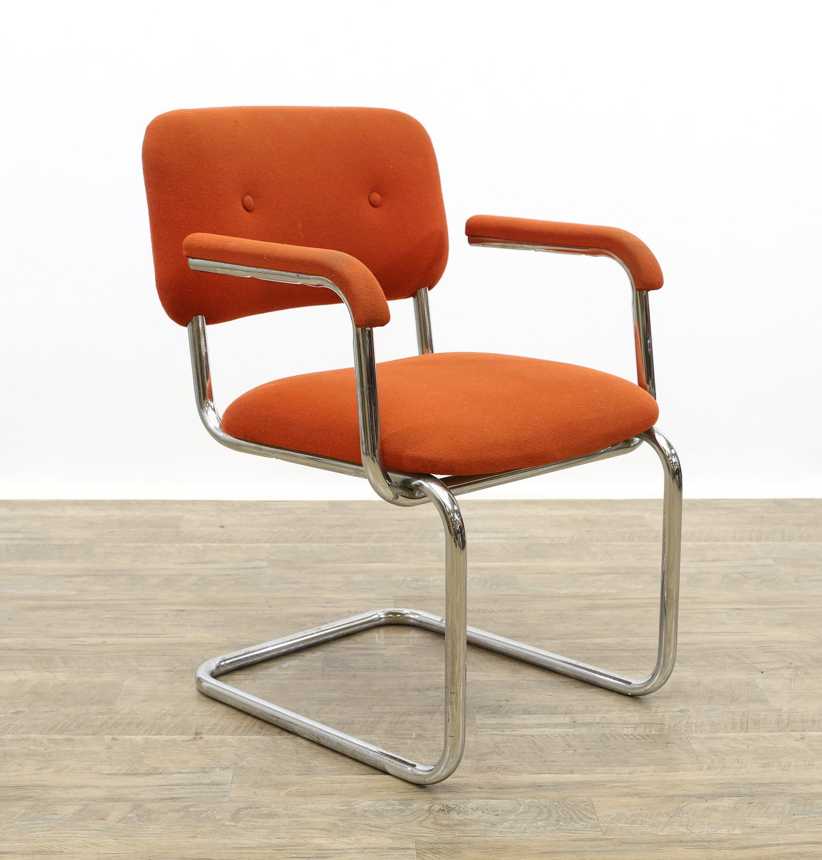 Cantilever Chair: Tubular steel chair in cantilever form with burnt orange upholstery, made by Fixtures Manufacturing. Some stains/wear to the upholstery and pitting to the metal. 32"h x 23"w x 21"d, seat height 17"