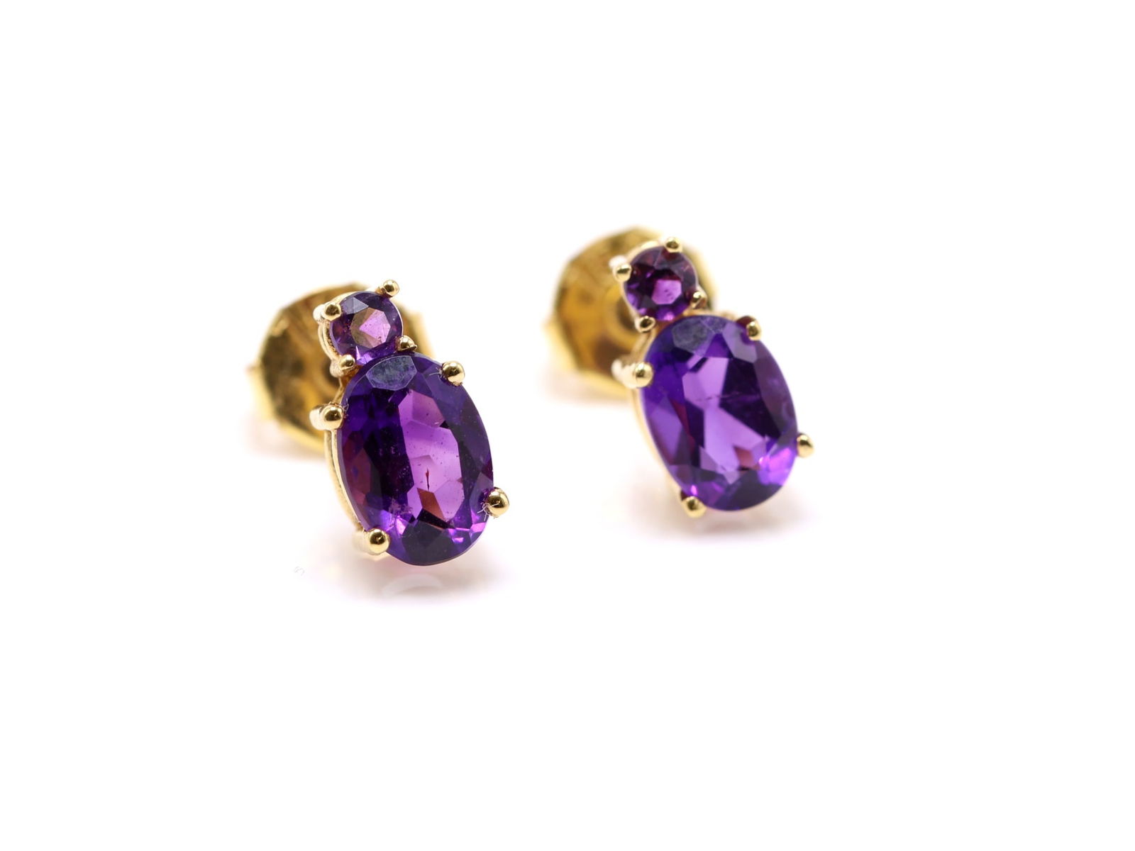 18k YG Amethyst Earrings: 18k yellow gold stud earrings set with oval cut amethysts totaling approx. 0.65 carat, each accented by a smaller round amethyst, approx. 3/8" and 1.2dwt