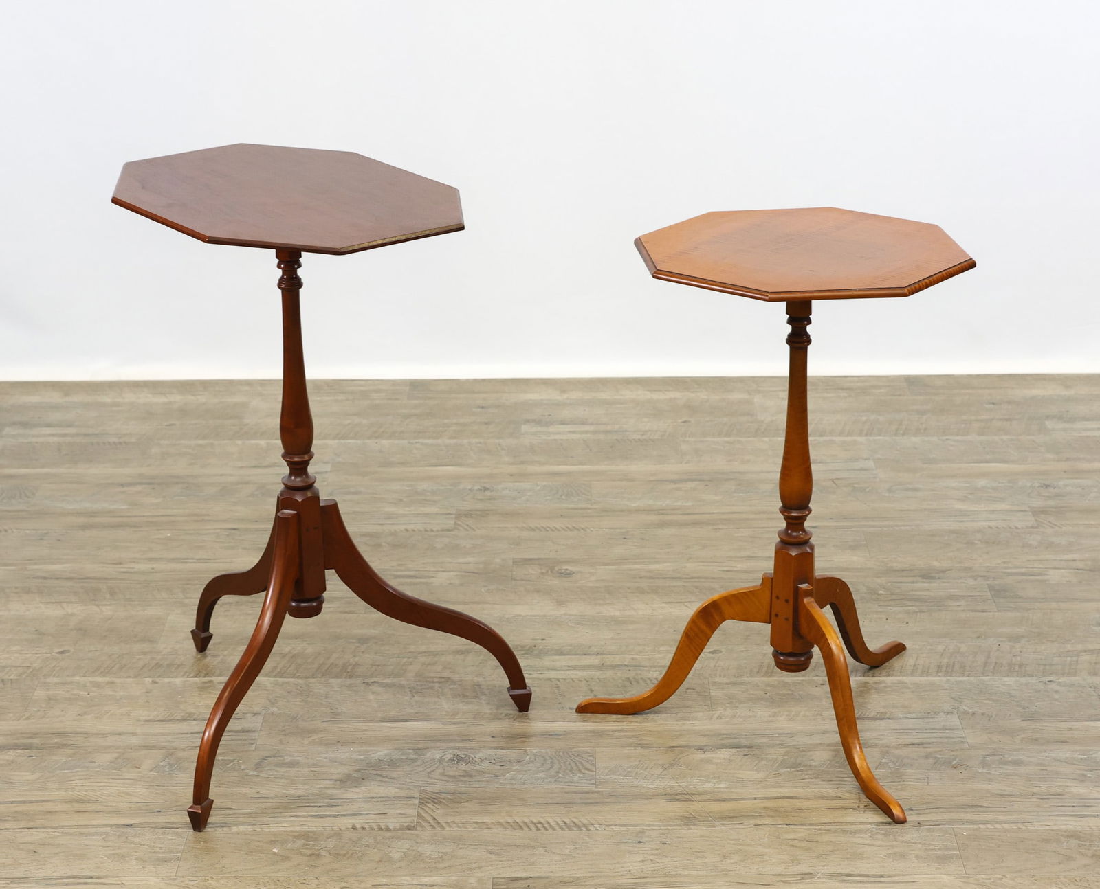 Eldred Wheer Hand-Crafted Candlestands: One tiger maple stand having and octagonal top, turned pedestal, cabriole legs and flat feet. One cherrywood octagonal tilt-top stand having a turned pedestal on spider legs with triangular feet.