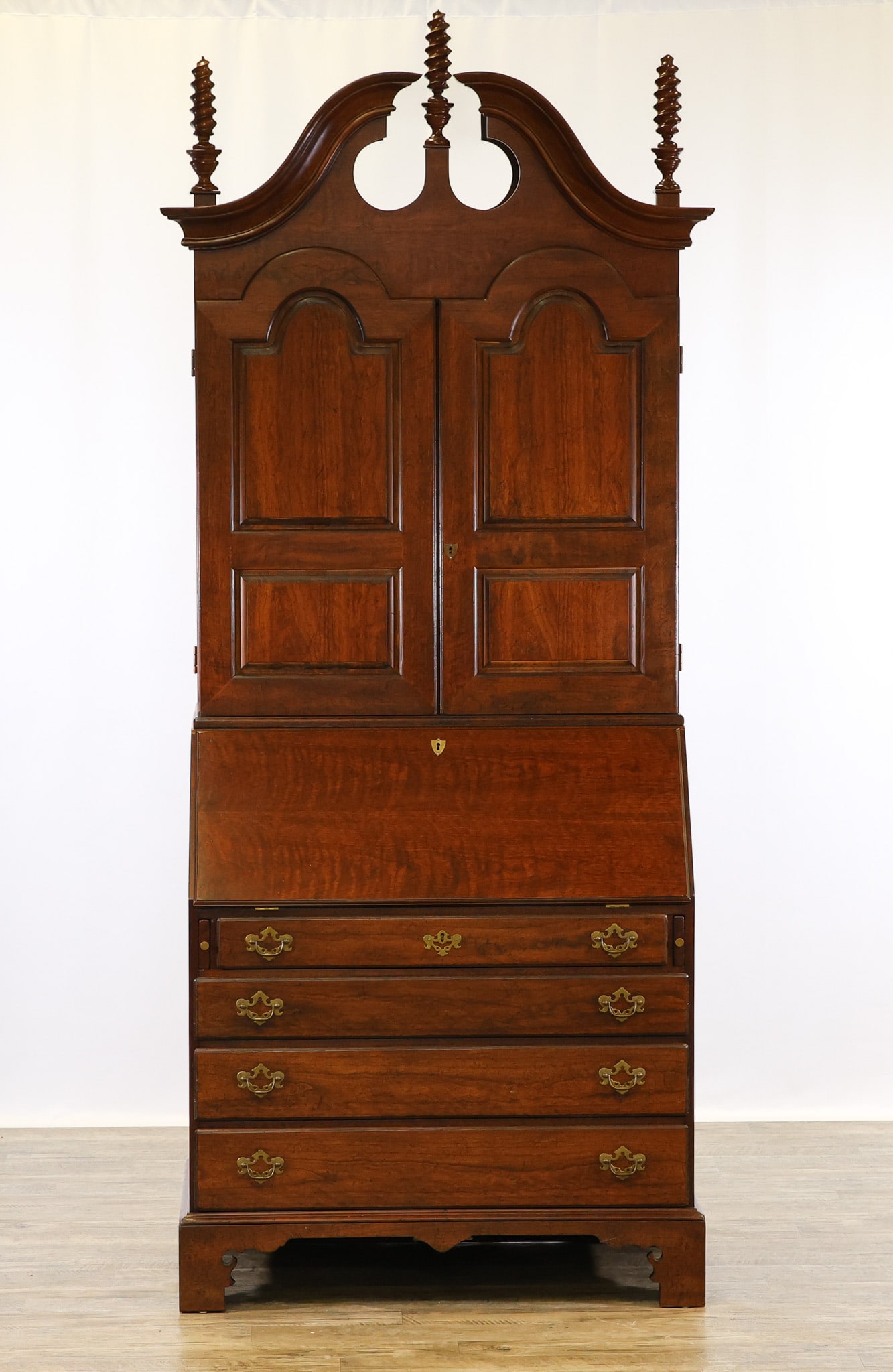 Wright Table Co. Secretary Desk: Two-part cherry case having a broken arch pediment with spiral flamed finials, arched blind two door top with fitted interior over a slant front desk with fitted interior over four graduated drawers