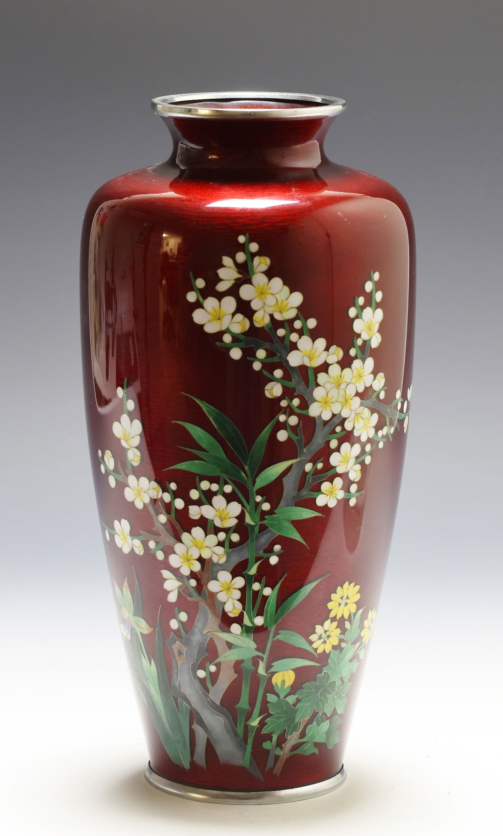 Ando Japanese Ginbari Cloisonne Vase: Taisho era silver wire cloisonne vase depicting cherry blossoms and other flowers over a red ginbari ground, with silvered mounts. Marked for Ando to the rim of the foot. 11"h x 5.25"w