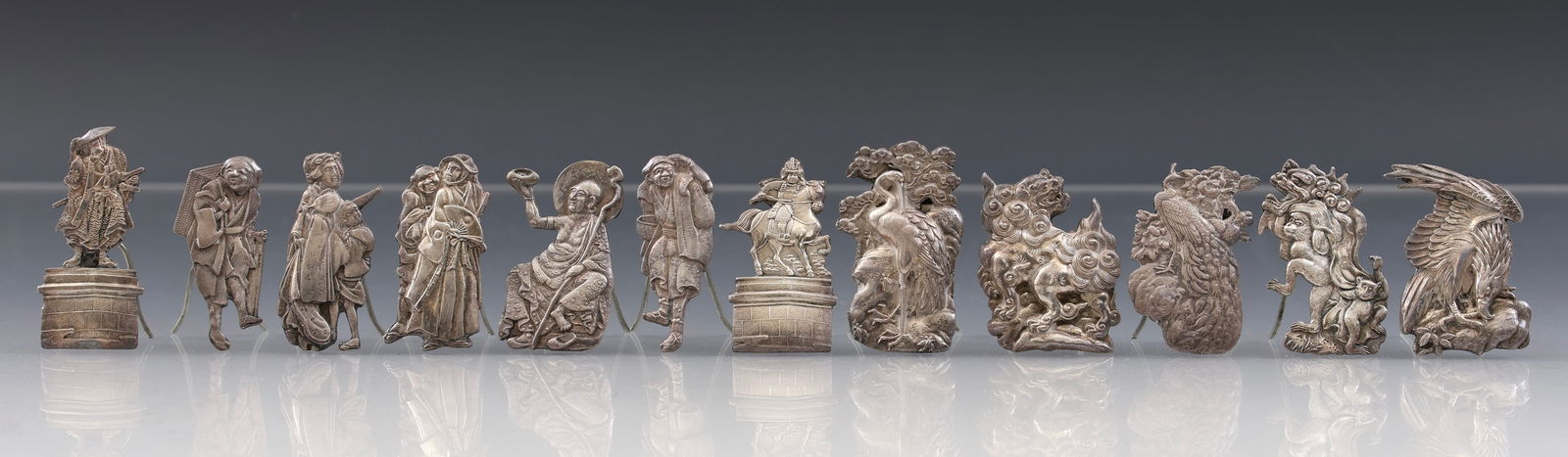 Japanese Silver Place Card Holders: Meiji - Taisho era place card or menu holders in the form of human and mythological figures, all stamped with the jungin / pure silver mark. (12) pieces. Each approx. 1.75"h x 1"w. 3.19 ozt