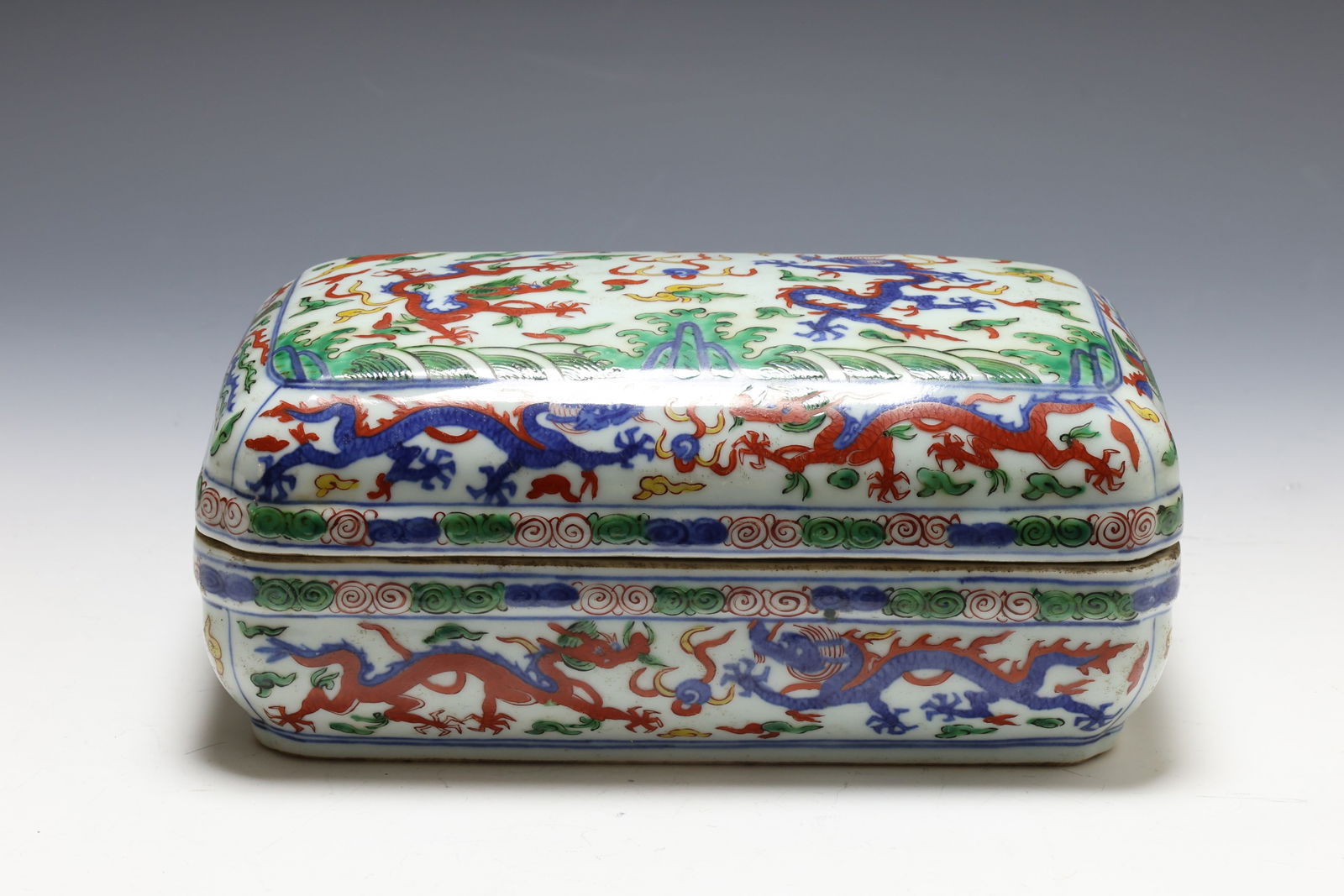 Chinese Wucai Porcelain Box: Qing era wucai porcelain box decorated with dragons chasing pearls, phoenixes, and cloud and water motifs. Jiajing reign mark to the foot. 4.25"h x 9"w x 5.5"d