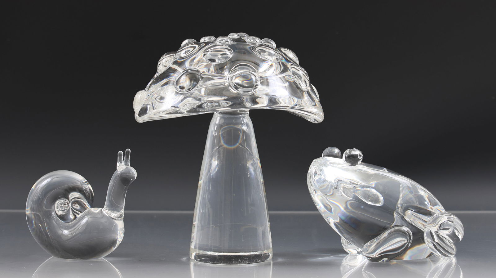 Steuben Crystal Woodland Figurines: Crystal figurines, including "Mushroom - Narrow/Mottled", model no. 8267, 6.5"h x 5"w, "Frog", model no. 8109, 3"h x 3.25"w x 4.5"d, "Snail", model no. 7982, 3"h x 1.25"w x 3.25"d. All marked for Steu