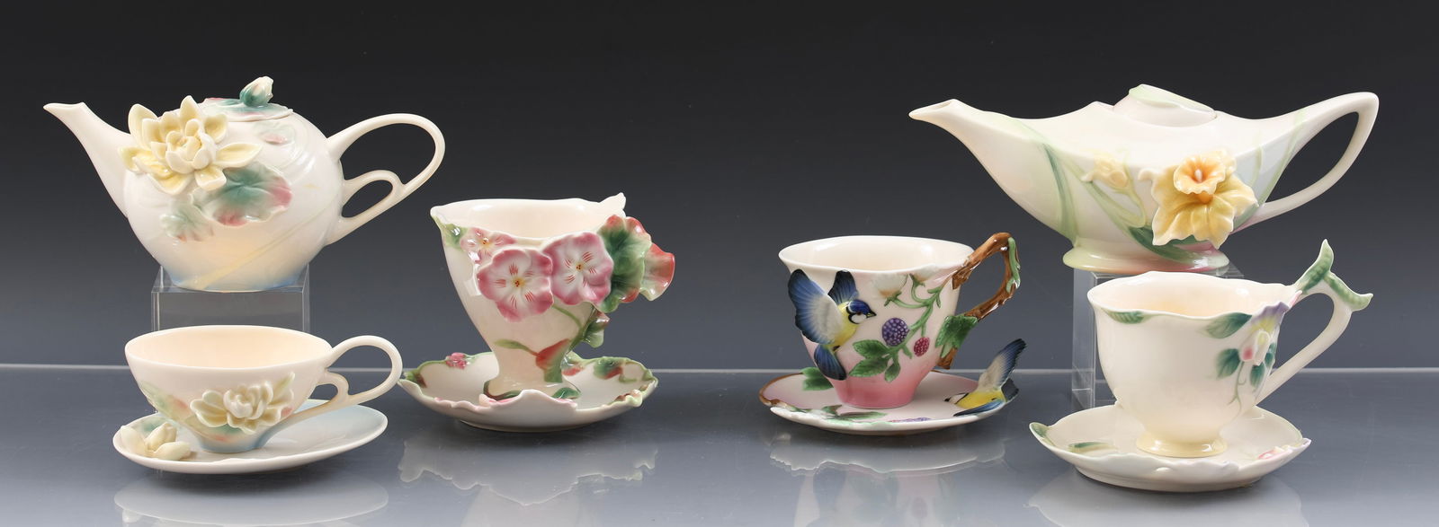 Franz Porcelain Teawares: Modern China wares, including a "Daffodil" teapot (3"h x 8"w), a "Water Lily" teapot (3"h x 6.5"w), teacup, and saucer, a "Blue Jay and Blueberry" teacup and saucer, a "Joyful Geranium" teacup and