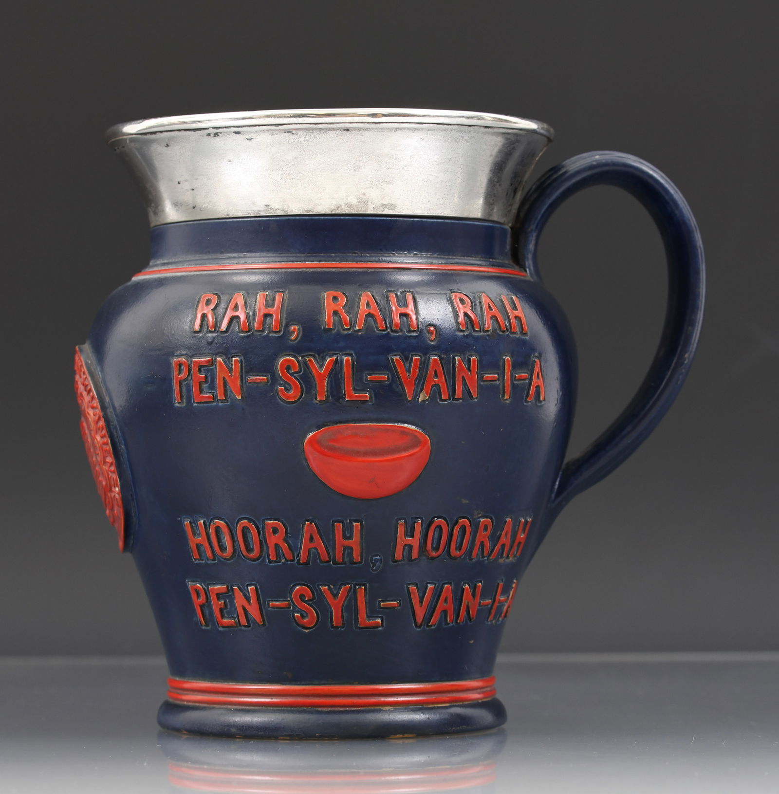 Doulton Pottery University of Pennsylvania Tankard: 19th C. U-Penn commemorative tankard by Doulton with a sterling silver rim marked for Birmingham, 1895, by Bishton & Fletcher. Raised decoration includes a college cheer, the university seal with