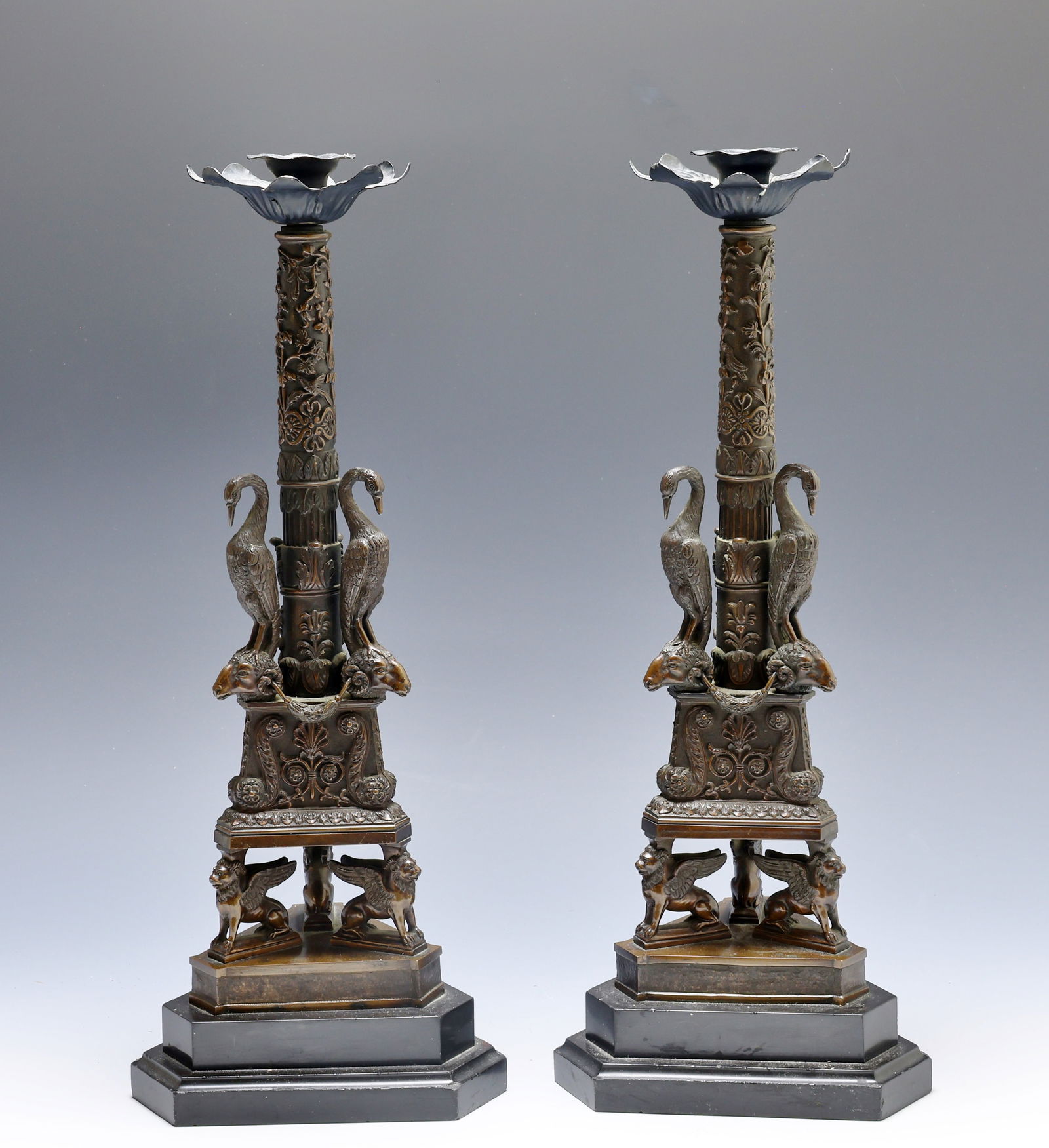 After Giuseppe Boschi (1760 - 1821) Bronze Candlesticks: Neoclassical bronze pair of candlesticks, with triangular bases featuring three winged lions supporting a platform which holds the stem, which is surrounded by three cranes perched on rams heads