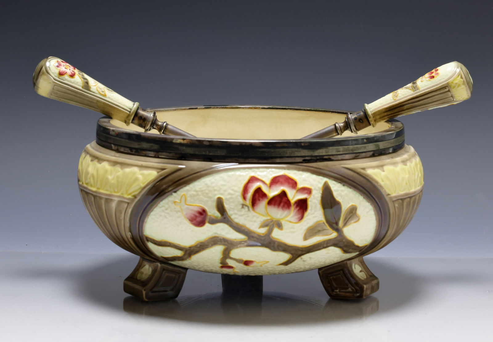 Wedgwood Majolica Bowl with Serving Utensils: Wedgwood majolica serving bowl raised on four feet, molded and enamel decorated with lotus blossoms and foliage and accompanied by a pair of matching handled servers. 5"h x 10"w and 11" length