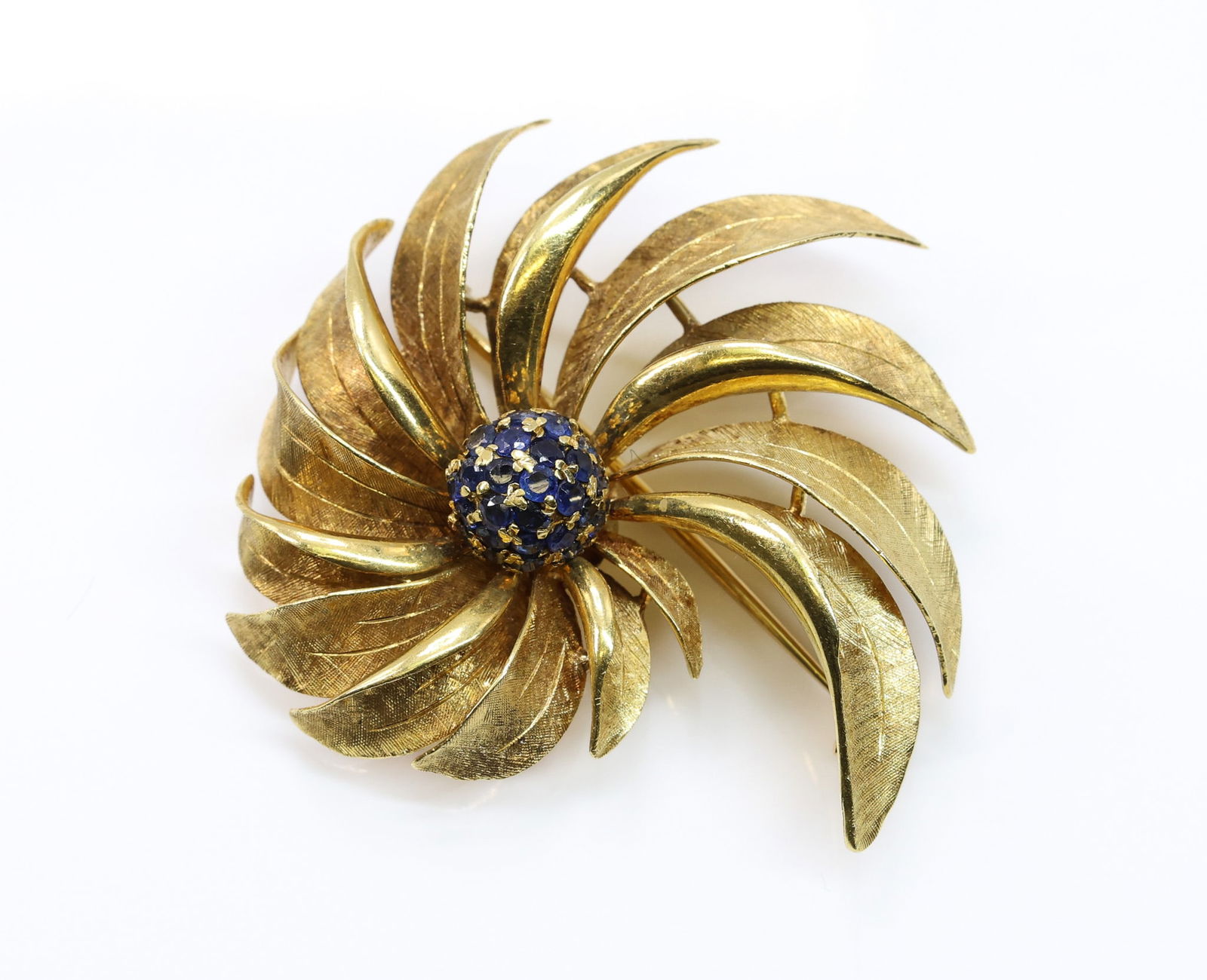 18k YG Sapphire Brooch: 18k yellow gold stylized foliate brooch set with a cluster of round cut sapphires. 1.5" w. 8.7 dwt.
