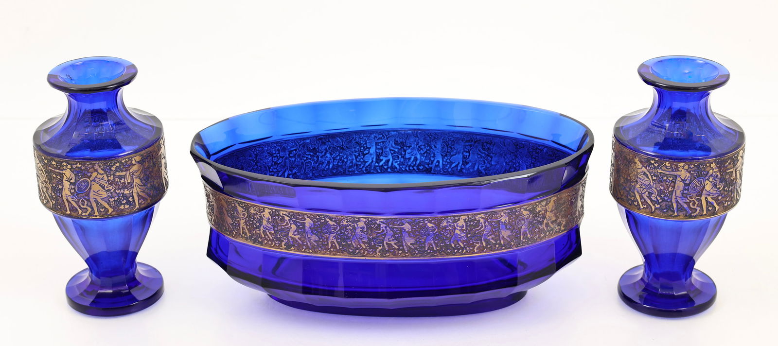 Moser "Sovereign" Cobalt Glass Garniture Set: Bohemian glass centerpiece bowl and pair of vases, faceted cobalt with gold intaglio friezes depicting mythological warriors, all with hand etched markings. There is a small chip on the foot rim of on
