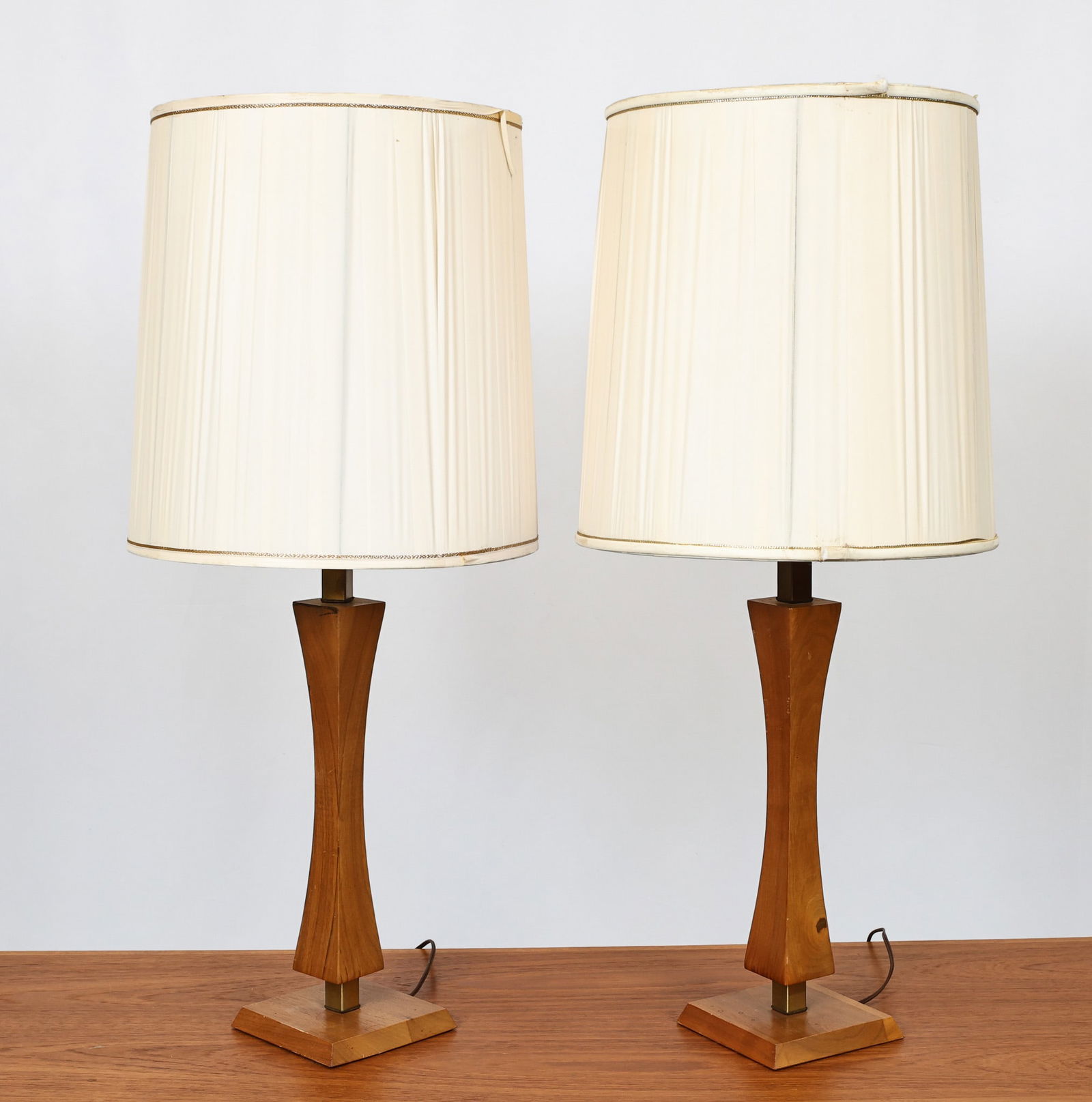 Teak and Brass Lamps: Danish Modern style pair of teak and brass table lamps of hourglass form with beveled square bases. Unmarked. In working condition. Surface wear including scuffs and discoloration. (2) lamps. Overall