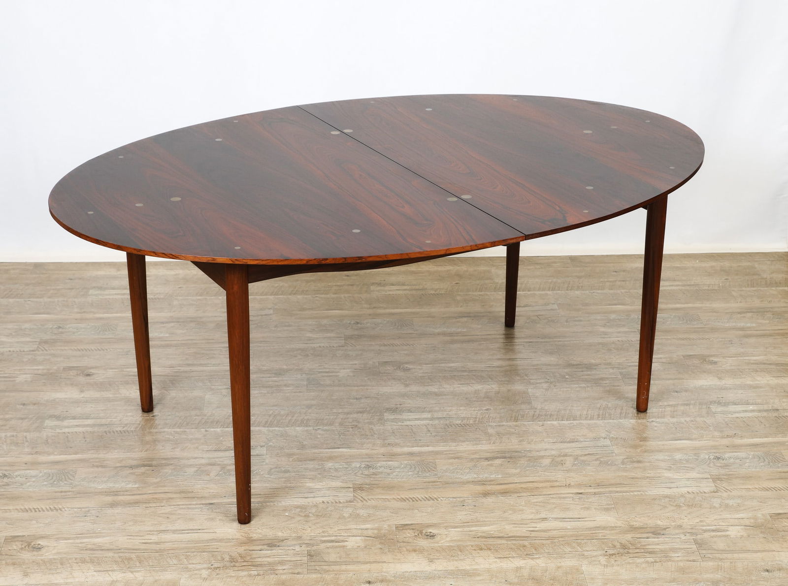 Finn Juhl for Niels Vodder "Judas" Dining Table: Danish Modern rosewood dining table with an extendable oval top featuring inset sterling silver medallions, with sculpted aprons, and raised on cigar legs. Originally known as the "Small Silver Table"