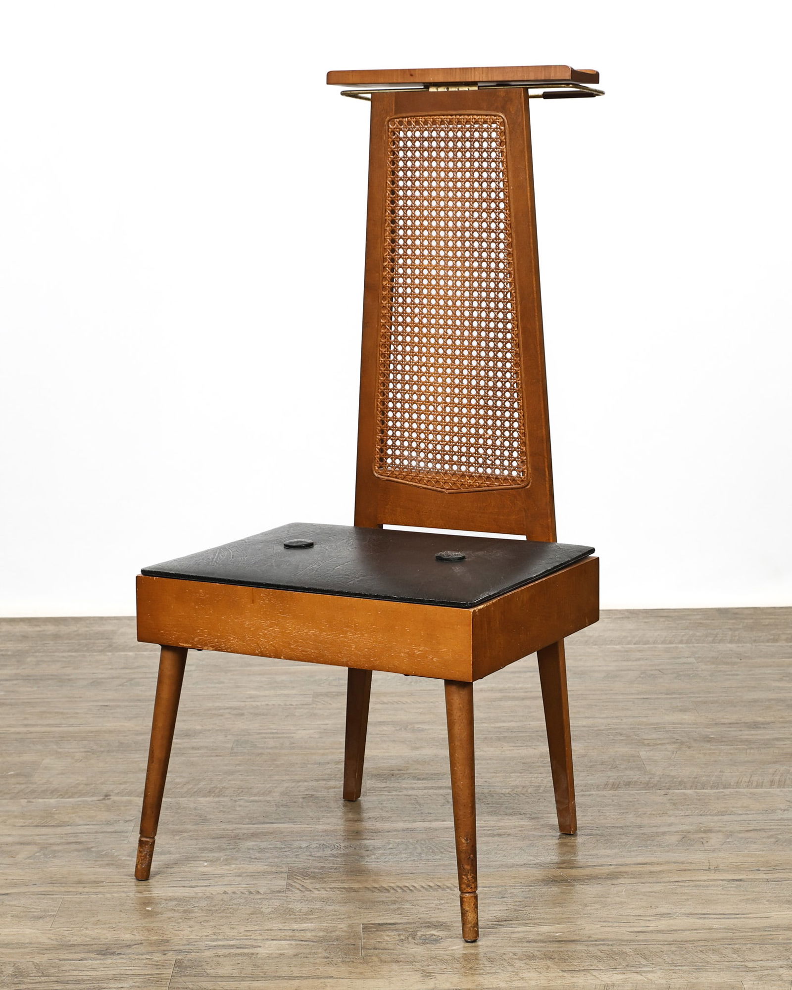 Pearl-Wick Valet Chair: Cane back and maple valet chair with an oversized seat featuring tufted black vinyl upholstery which lifts to a storage space, the top of the tapered back with a small shelf and brass rail for hanging