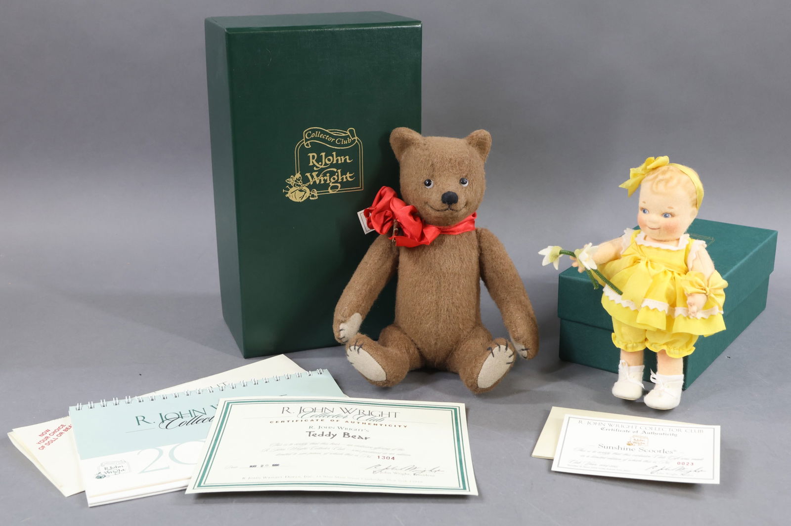 R. JOHN WRIGHT.: Pair of MIB Collector's Club items. 6 1/2" 2004-2005 "Sunshine Scootles" Doll. 0023/. COA. 9" 1998 "Teddy Bear", 1304/2500. COA. 2004-2005 Collector Club Calendar. This lot is being sold AS IS.
