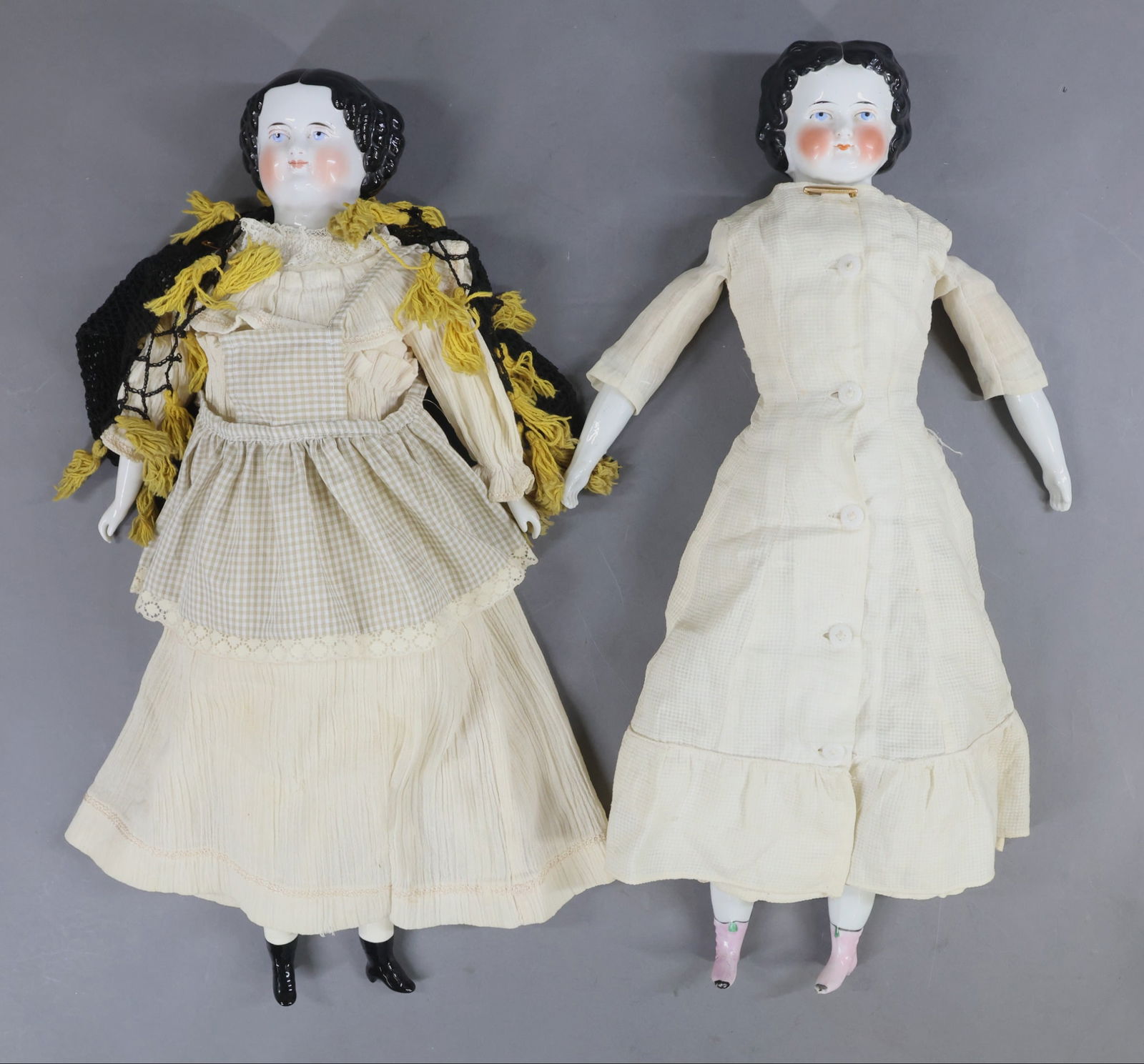 CHINA DOLLS.: Pair of antique dolls with center part black hair, painted blue eyes, rosy cheeks. They are both wearing cotton clothing. Doll 1) 20" has an antique cloth body with china lower arms and legs, pink