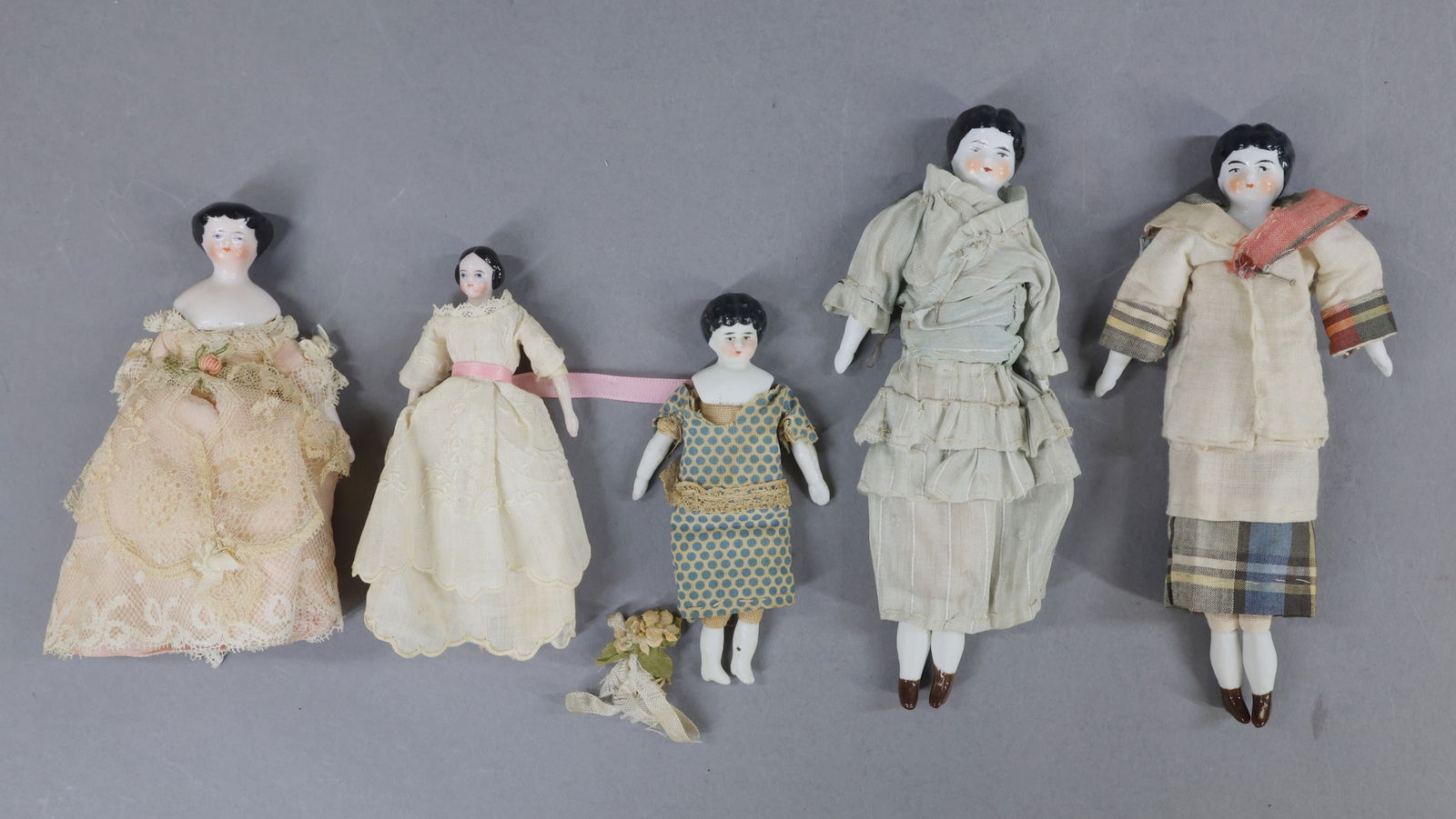 MINIATURES - DOLLS.: LOT of (5) China dolls. 3 1/2" - 6". (3) Low Brows. Flat top style. Center part. All have black hair, (2) have a faint pink tint. Cloth bodies with china lower limbs. Vintage/antique clothing. (4) Sta