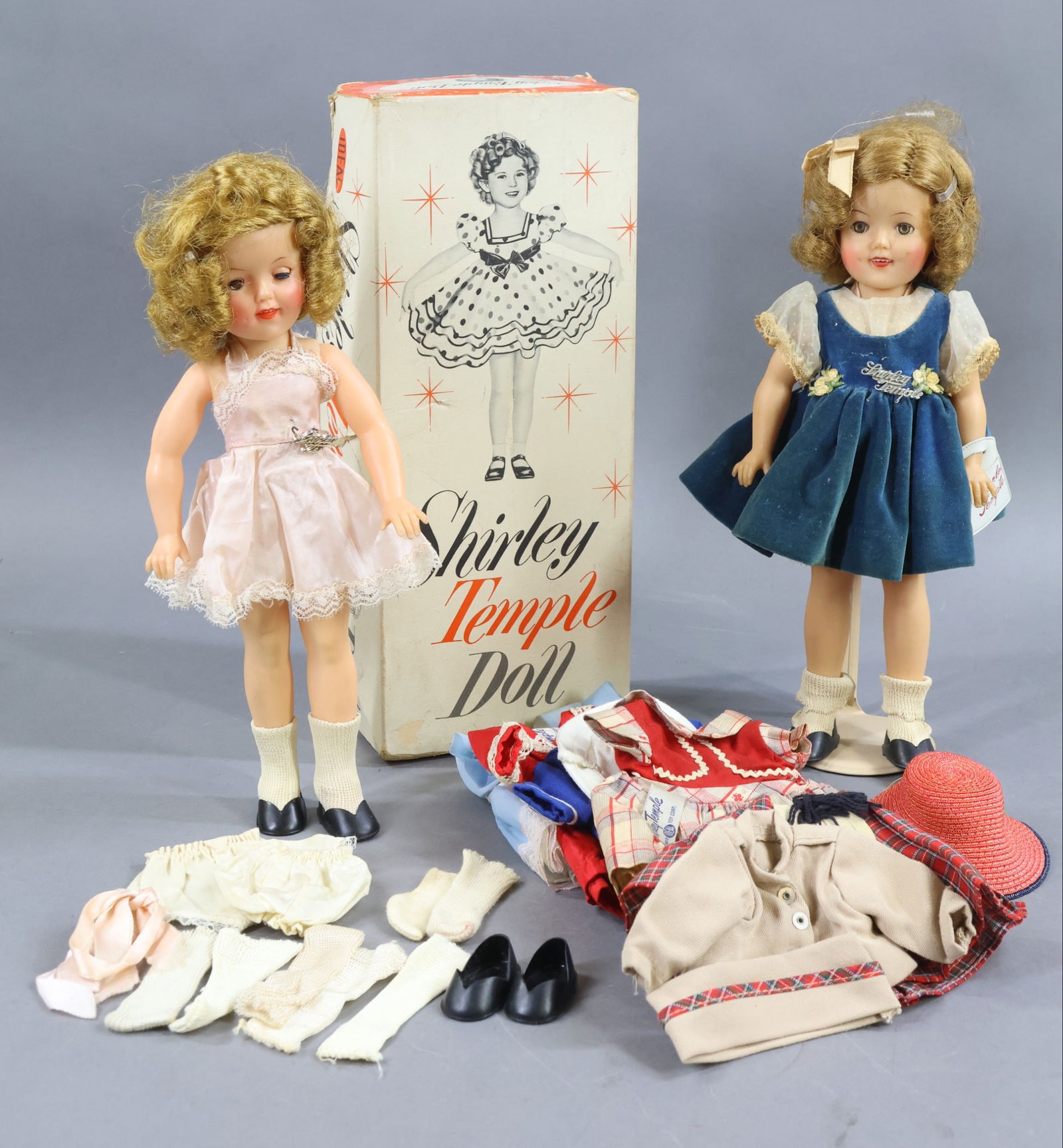 1940's-1960's DOLLS.: Pair of 12" 1957 IDEAL "Shirley Temple" vinyl dolls, clothing. Both dolls have their logo pins. Hair is uncombed but played with. (1) Doll is in an OB. They come with (6) tagged outfits, (3) prs. of