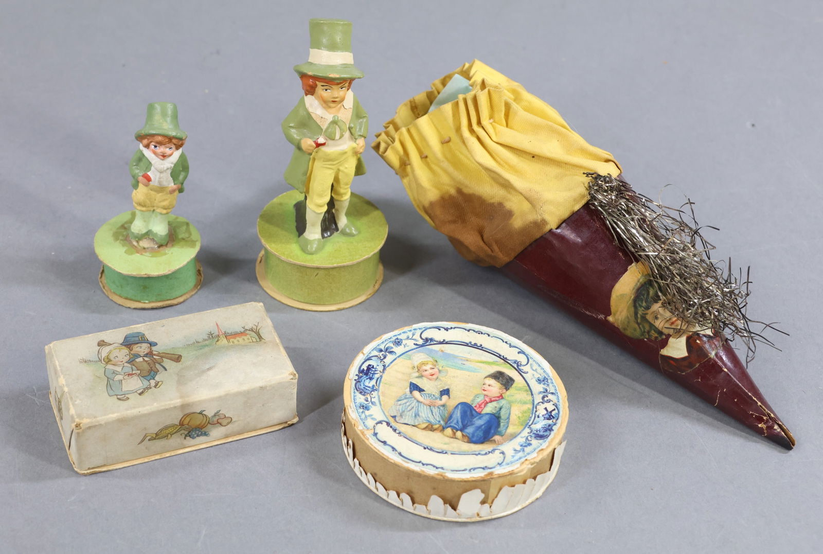 HOLIDAY/NOVELTIES.: NOVELTY. Lot of (5) antique Candy Containers/boxes. 7" Cloth and paper cone with tinsel/scrap decoration. (Age discoloration.) Pair of papier mache Irish fellas each standing on a round box. 3", 4