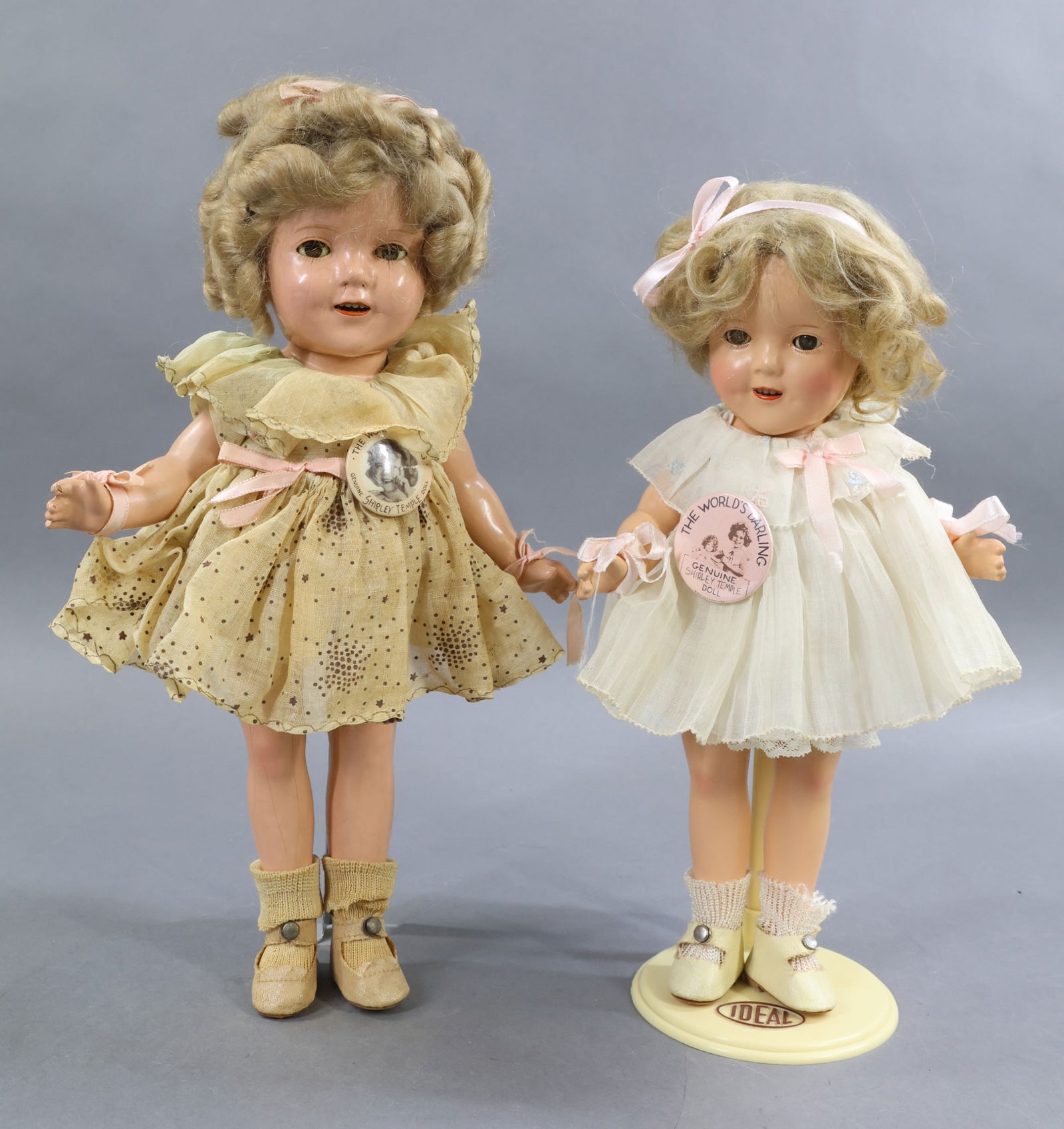 COMPOSITION DOLLS.: Pair of IDEAL "Shirley Temple" dolls dressed in original clothing. Both have their original honey blonde mohair wigs, original "The World's Darling" pins. Both have 1 pc. undergarments, ivory