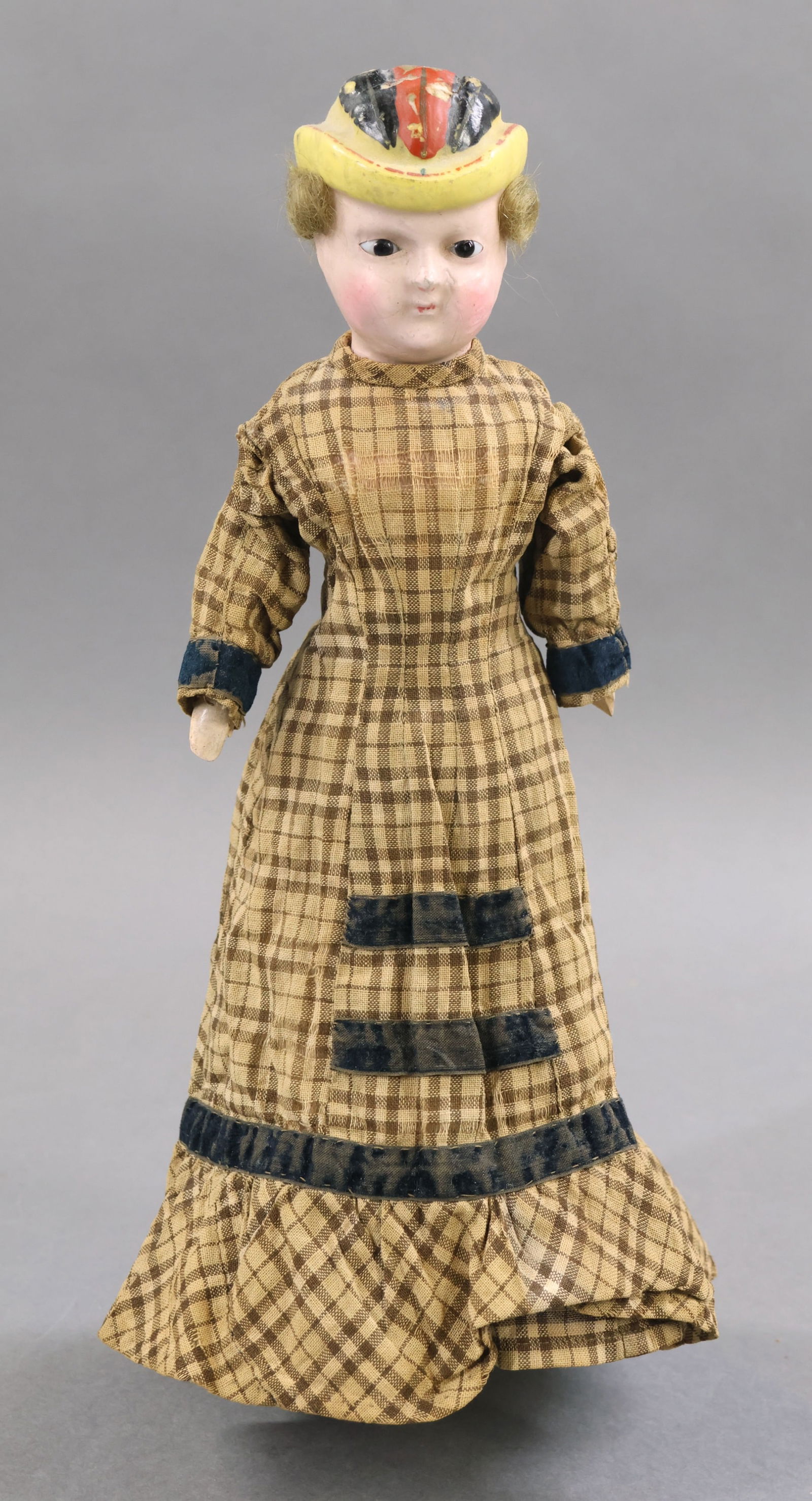 PAPIER MACHE/WAX OVER.: 12" Ca. 1860 Wax over papier mache Bonnet shoulder head doll with stationary black eyes, honey blonde mohair wig. Molded yellow bonnet with painted feathers. Cloth body with wooden lower arms and