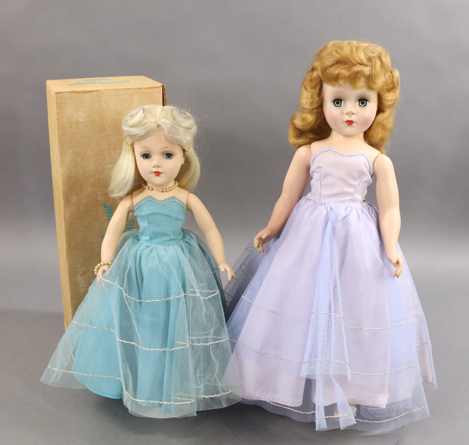 1950's-1960's DOLLS.: Pair of MARY HOYER hard plastic dolls with blue sleep eyes and dressed in very similar tagged strapless taffeta gowns with silver trim. 18" "GiGi" with a honey blonde wig. Pale blue tulle over pale la