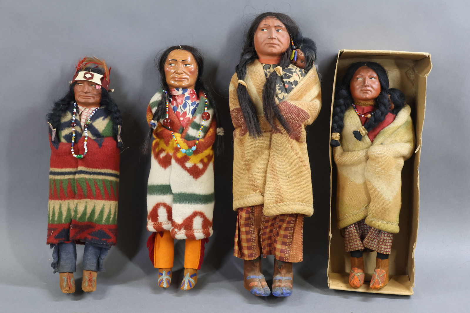 NATIVE AMERICAN DOLLS.: LOT of (4) all original SKOOKUM dolls. Late 1930's- early 1940's. All of the dolls have leather moccasins. (3) Of the dolls have oval labels on their soles. Marked - 13" Squaw with papoose in a