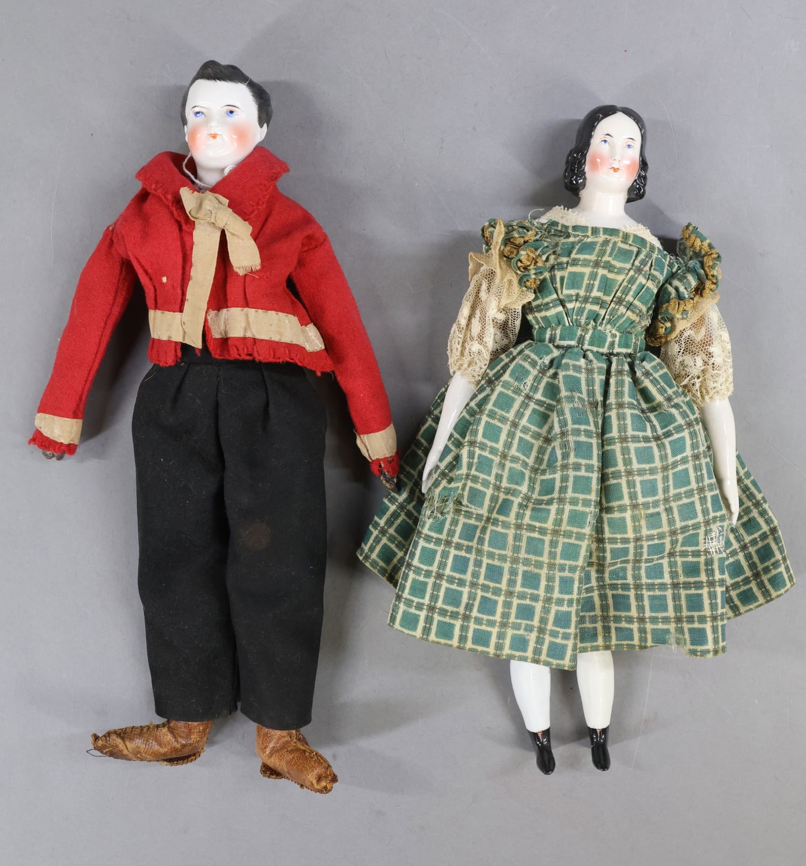 CHINA DOLLS.: Pair of unmarked dolls. Both dolls have painted blue eyes, rosey cheeks, black hair and are dressed in antique clothing. Female doll - 1870's-80's 12" with center part hair, long curls. Cloth body