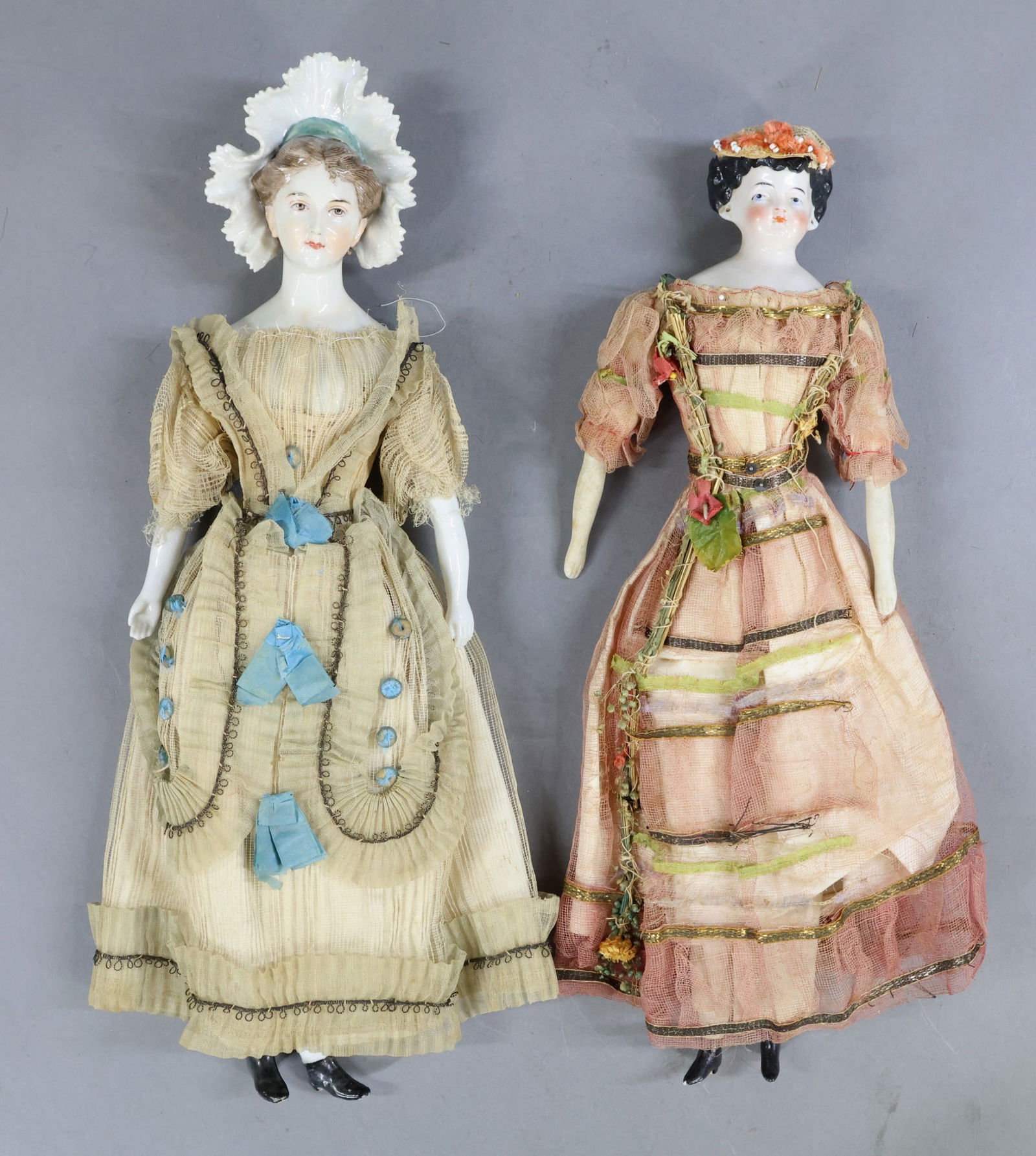 CHINA DOLLS.: Pair of dolls, dressed in what appears to be factory original clothing. Both dolls have painted pale blue eyes. 14 1/2" Doll 1) has a molded bonnet and pretty brown hair with individual brush