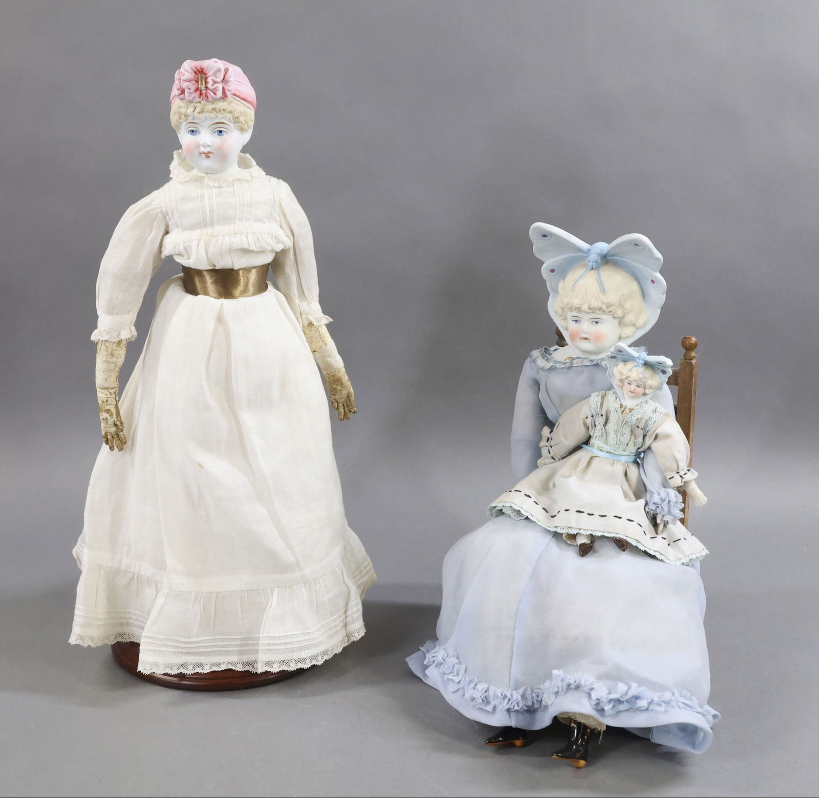 PARIAN/CHINA DOLLS.: LOT of (3) Parian dolls with molded, painted hair/hats, features. All of these dolls have blue eyes, blonde hair. Doll 1) 16" "3" with molded shirtwaist with gold bead necklace. Pink hat decorated wit
