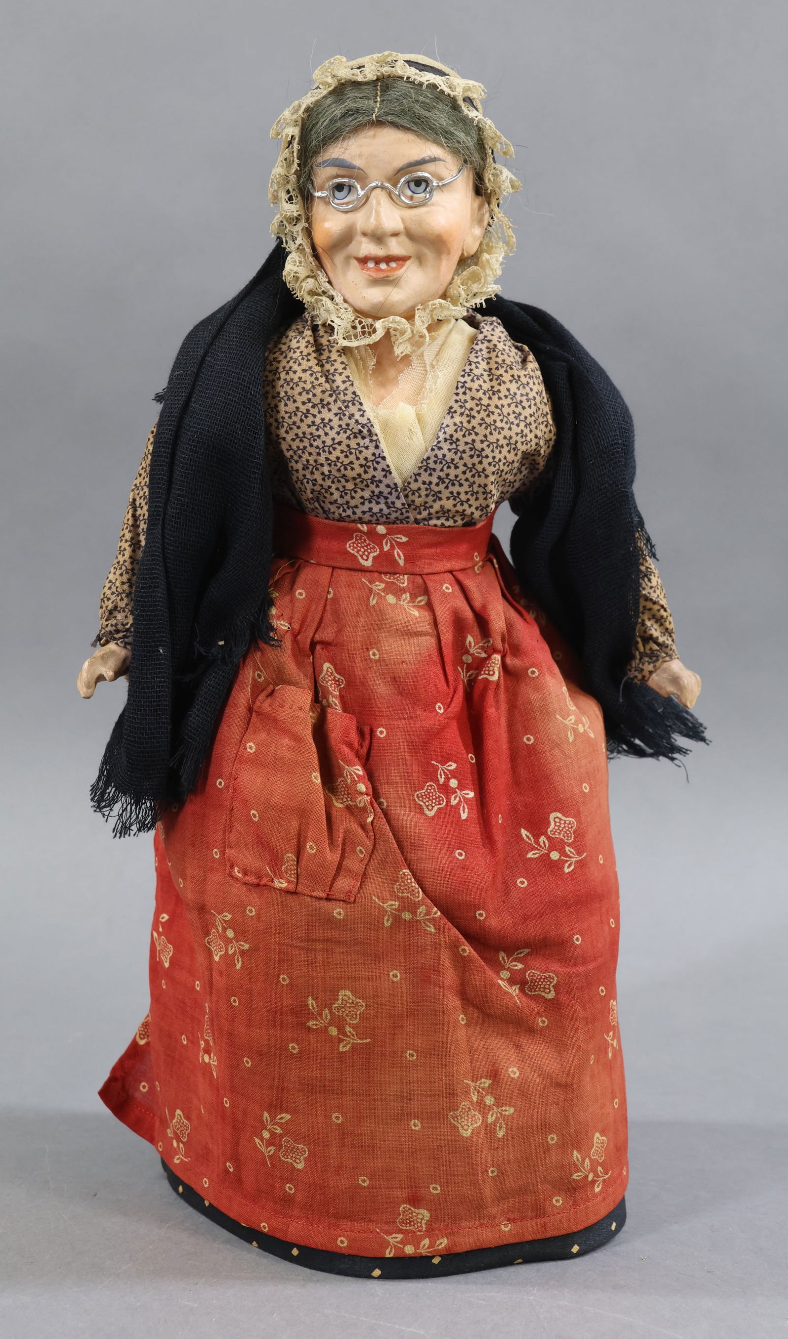 ANTIQUE PEDDLER.: 12" German 1870's Papier Mache Shoulder Head Lady Peddler Doll. Painted blue eyes, open/closed mouth with painted teeth. Grey mohair wig. Metal wire rim glasses. Cloth body with papier mache lower