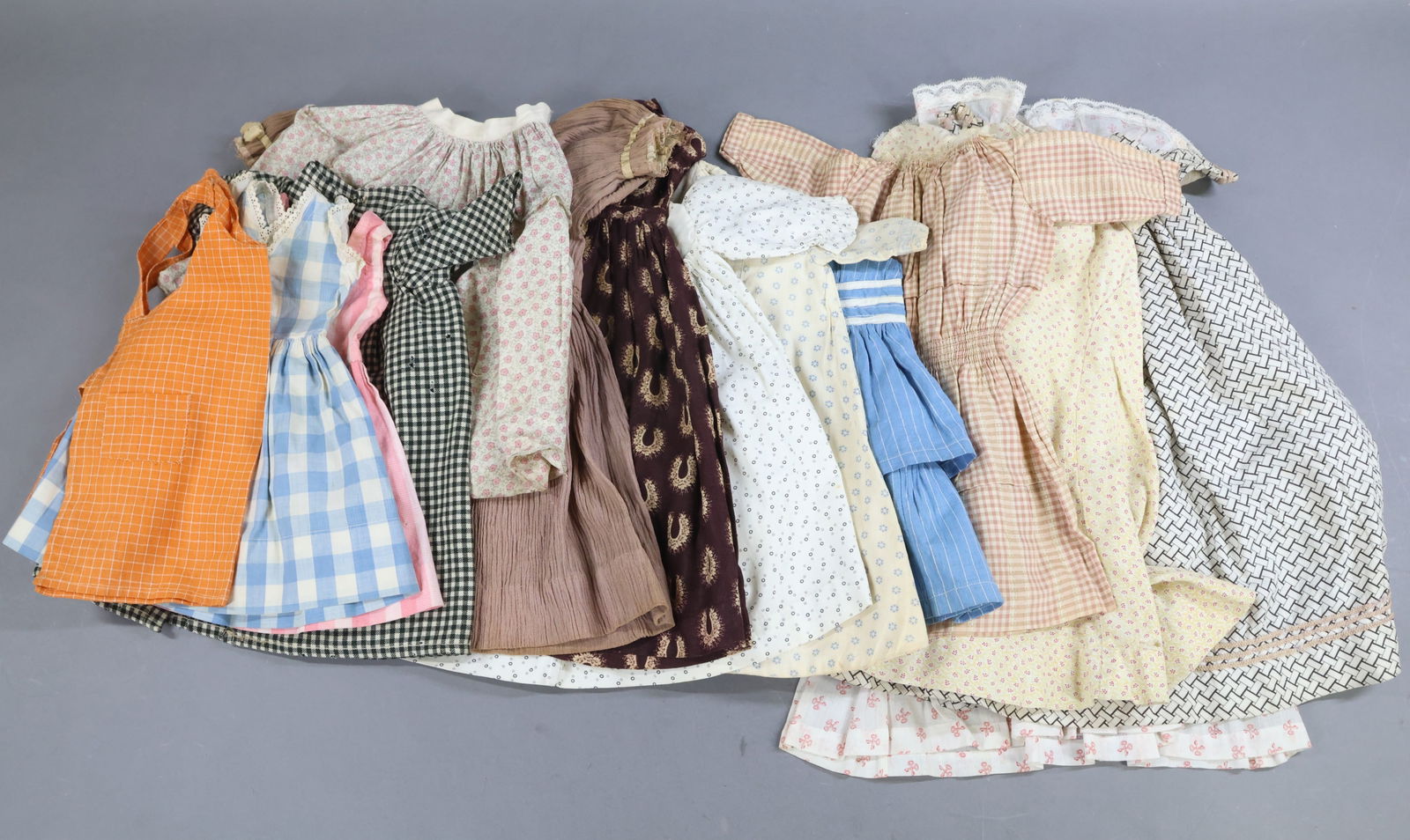 ANTIQUE CLOTHING, ACCESSORIES.: LOT of antique DOLL clothing. (8) Early cotton print dresses 14" - 19" L. (1) 14" Solid cotton dress . 11" Cotton print skirt. Plaid pinafore. (2) 1930's-40's Cotton dresses. 13" Wool check coat