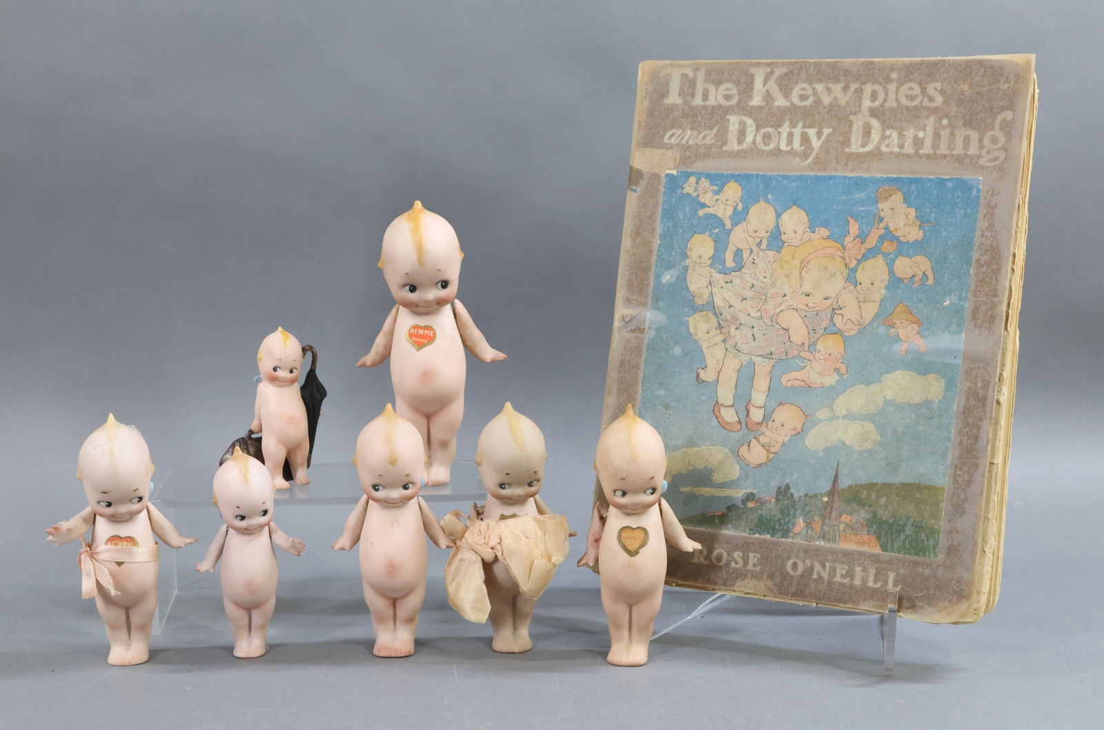 ALL BISQUE DOLLS.: LOT of antique KEWPIES. (1) 3 1/2" Action Kewpie with round paper label on back. Dated on bottom 10/17/1915. (6) Standing Kewpies with painted blue wings, strung arms. 4 1/4", 5", 5 1/4", 6" . (1) 5"