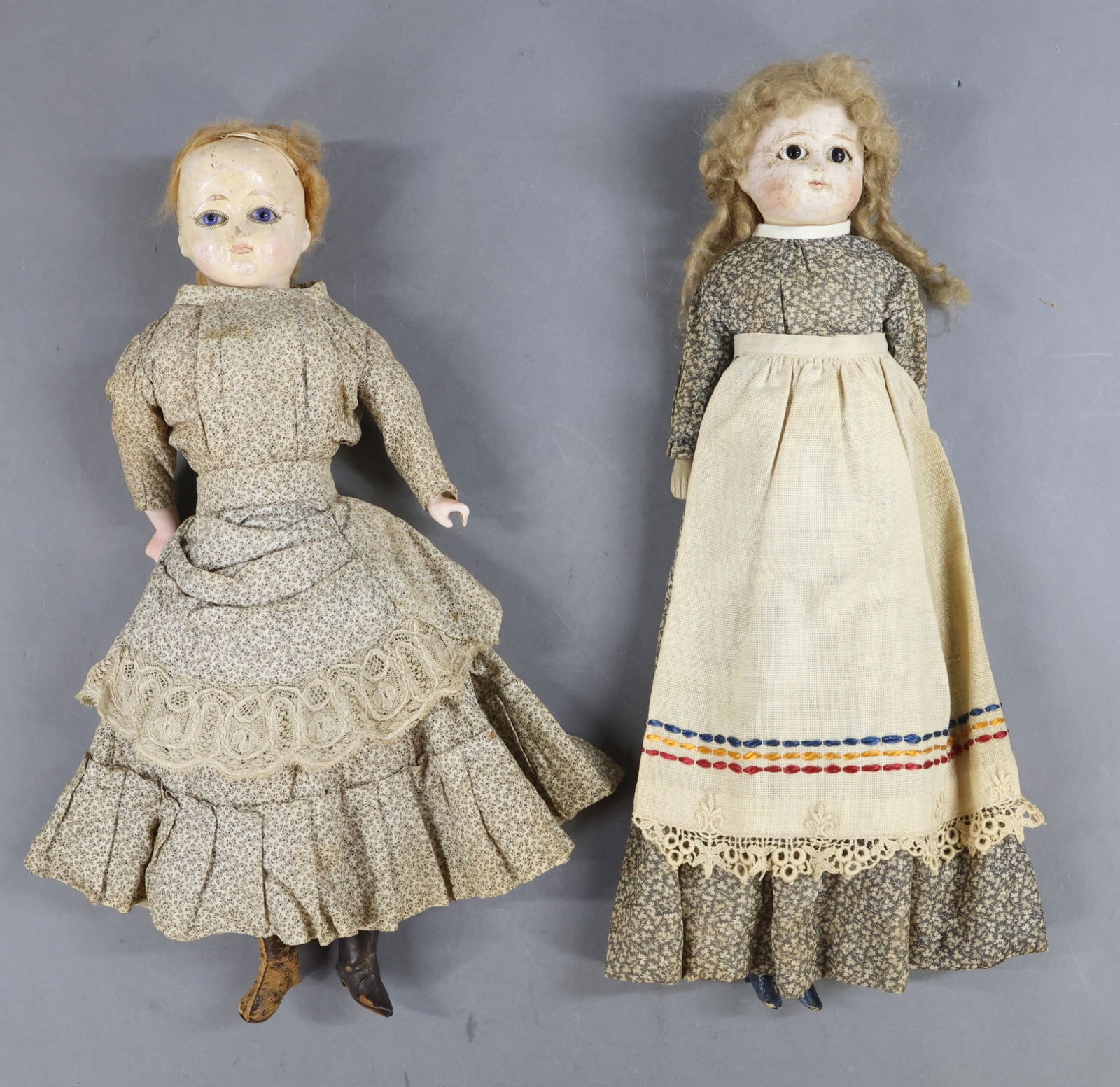 PAPIER MACHE DOLLS.: Pair of unmarked shoulder head dolls with stationary glass eyes, closed mouths, honey blonde mohair wigs. Both dolls are wearing antique cotton clothing. Doll 1) 14 1/2" has black pupil-less eyes.
