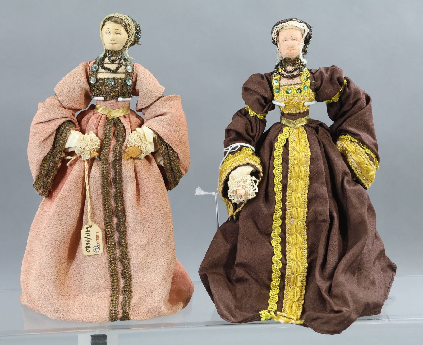 LIBERTY OF LONDON.: Pair of "Anne of Cleaves" dolls - 4th wife of King Henry VIII. Doll in brown is unmarked, doll in rose is tagged. (2) Stands. Condition: age fading, discoloration. This lot is being sold AS IS.