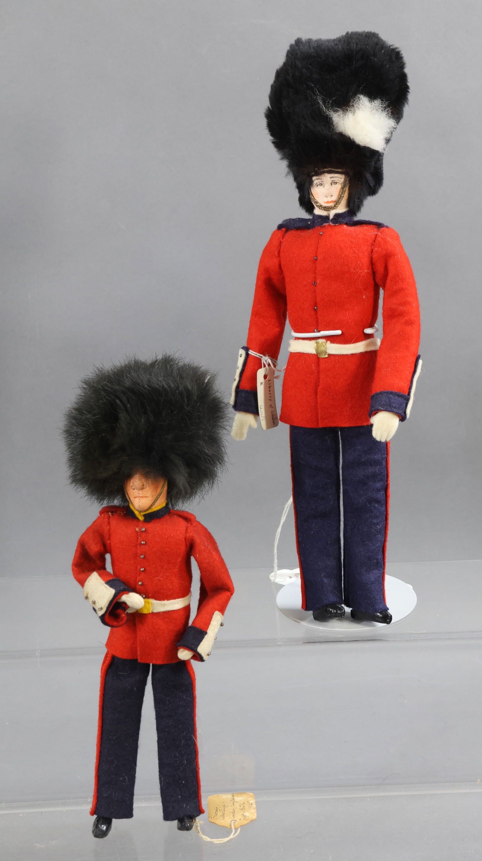 LIBERTY OF LONDON.: Pair of male dolls. 9" Unmarked "King's Guard", England 1935. Center seam. 11" Tagged "Grenadier Guard". (2) Stands. Condition: minor age discoloration on 9" doll. This lot is being sold AS IS.