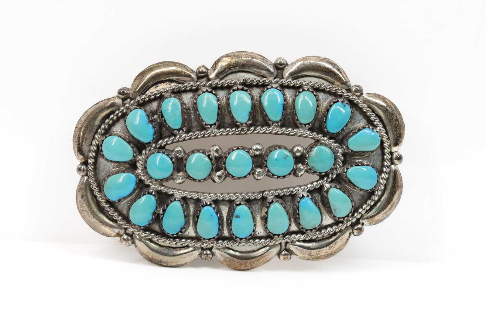 Navajo Sterling Silver Turquoise Buckle: Sterling silver belt buckle set with turquoise cabochons in a scalloped oval form with rope twist and bead decoration, likely Navajo, signed HV. 2.5"l x 1.75"h and .9ozt.