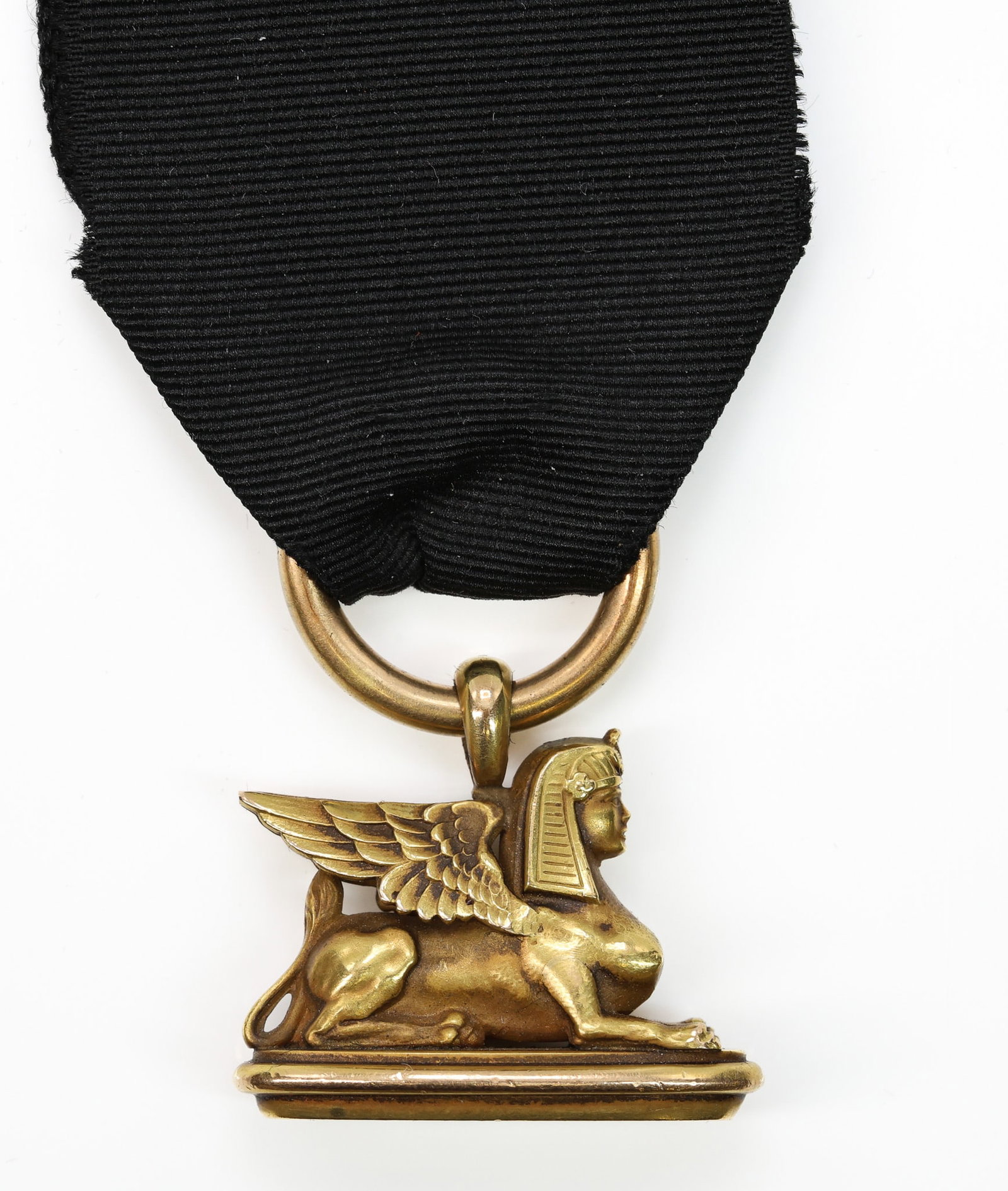 14k YG Sphinx Pendant Fob with Ribbon: 14k yellow gold pendant fob featuring a sphinx motif, suspended from a black ribbon with gold tone clasp, engraved base. Total weight 8.8dwt including ribbon.