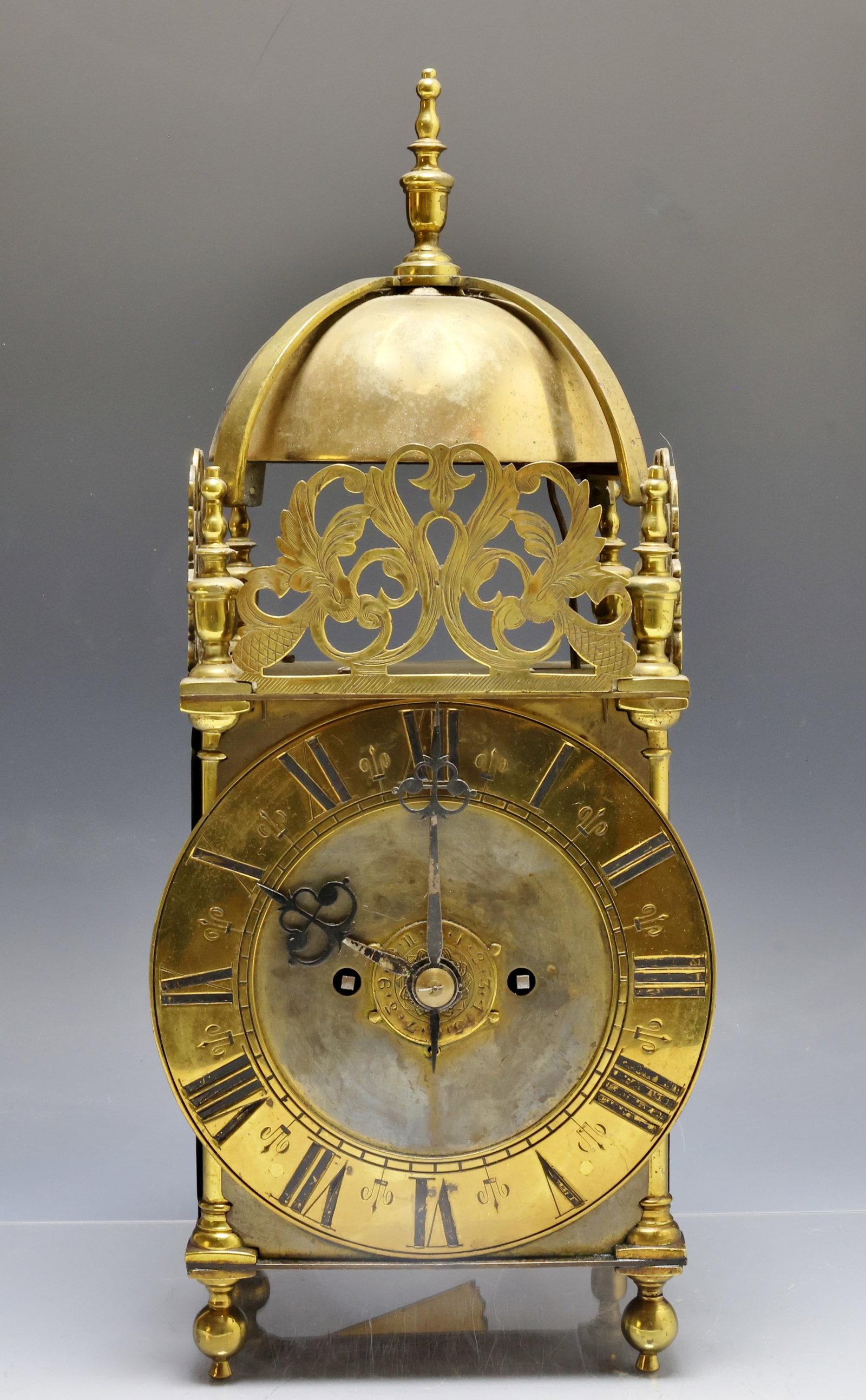 19th c . English Lantern Clock: Brass case with a top finial, dome bell, pierced foliate fretwork crest, sqaure bras sides supported by turned colunms on ball feet. Brass 8-day spring driven movement with double fusee. One foot has